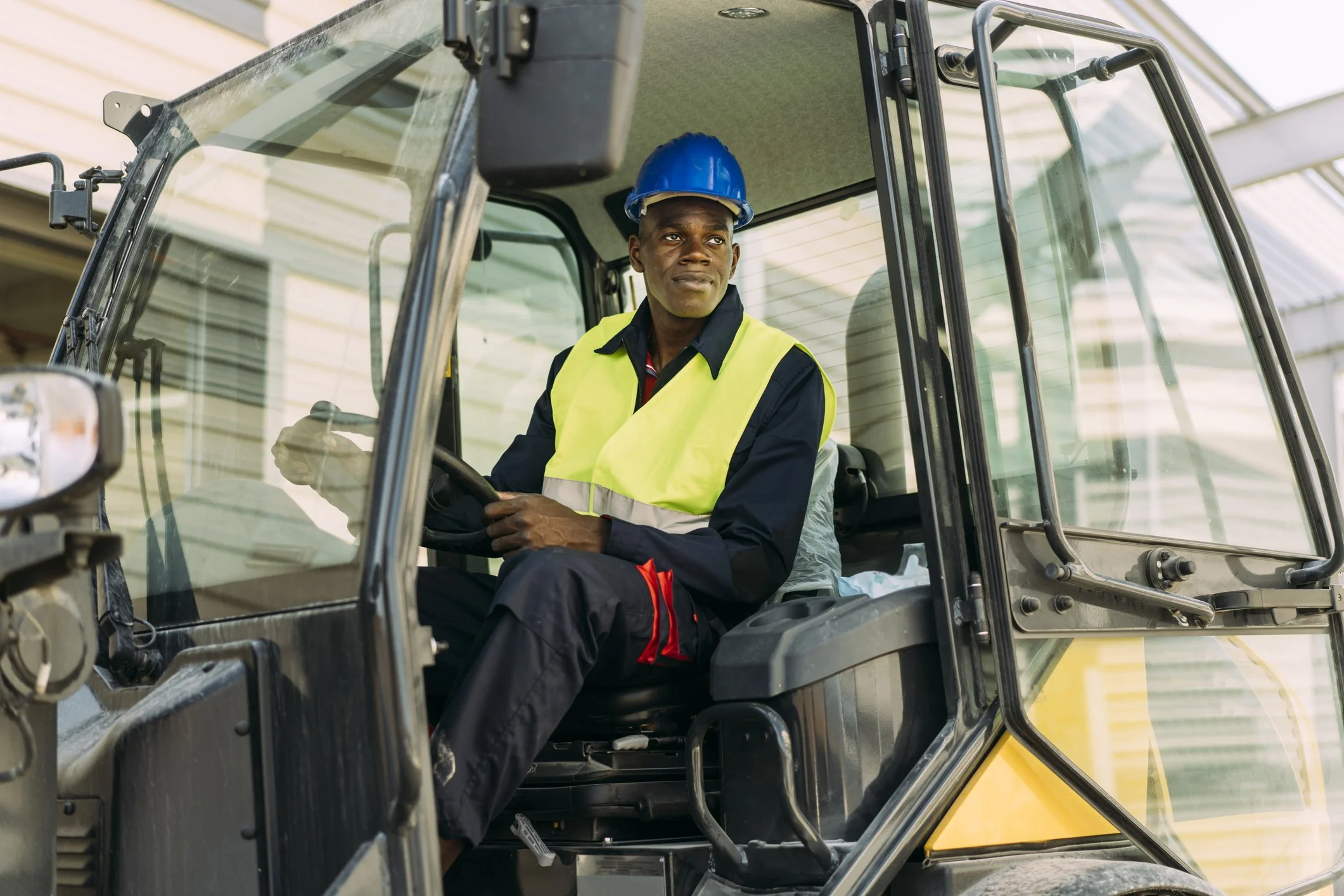 Man wearing a blue hard hat and yellow safety vest operates a construction vehicle.
