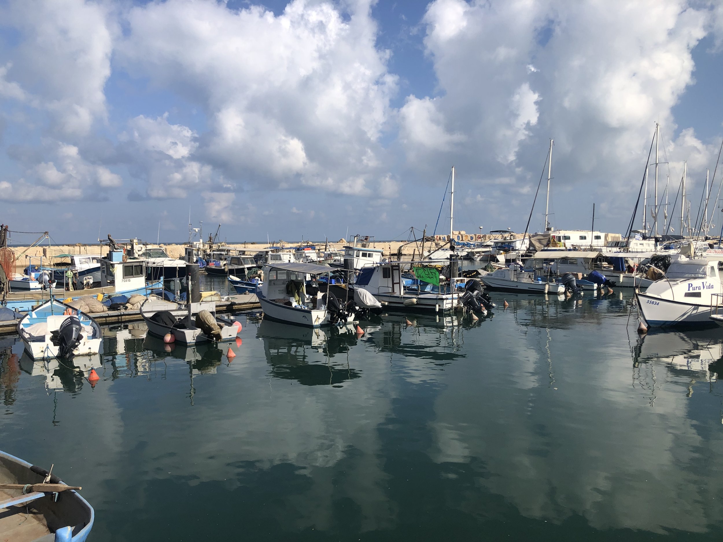 Fishing boats in a Mediterranean harbor with a lone fisherman, symbolizing reflection, readiness, and the beginning of a personal journey.
