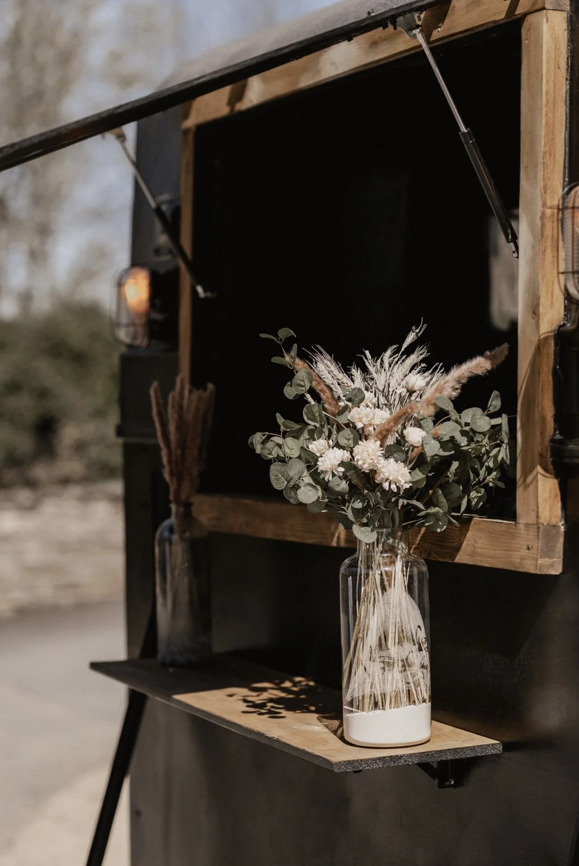 Vase mit getrockneten Blumen vor einer schwarzen Holz-Wand.