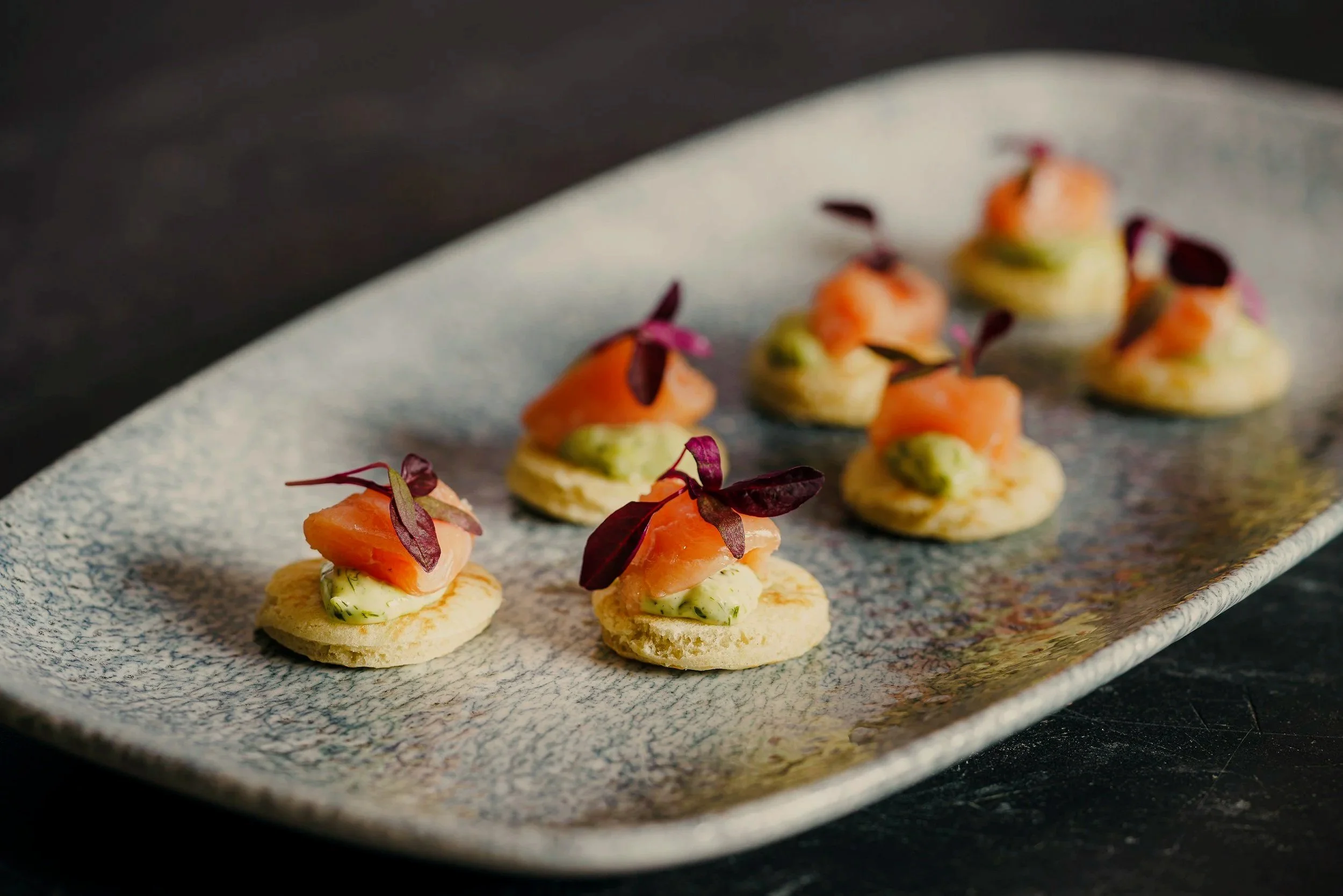 Kleine Canapés mit Lachs, Gurke und roten Blättern auf einem rechteckigen Teller