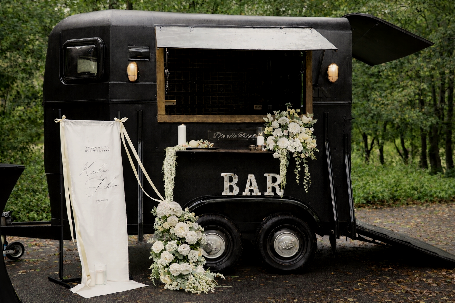 Ein schwarzer, kleine Food-Truck, dekoriert für eine Hochzeit mit weißen Blumen und Kerzen