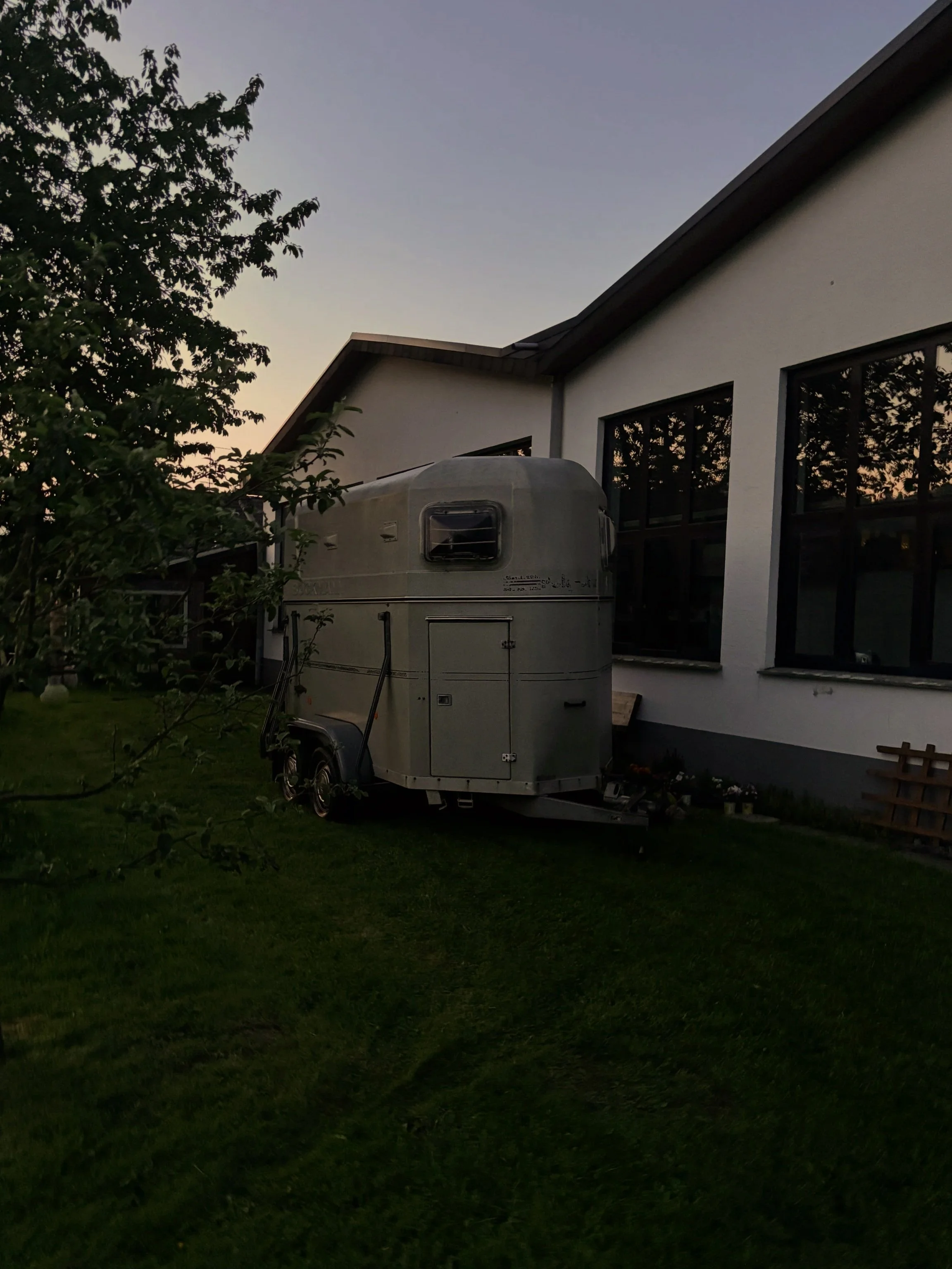 Ein Carport mit einem Wohnmobil davor, im Garten eines modernen Hauses bei Sonnenuntergang, viele Bäume und grüne Rasenfläche