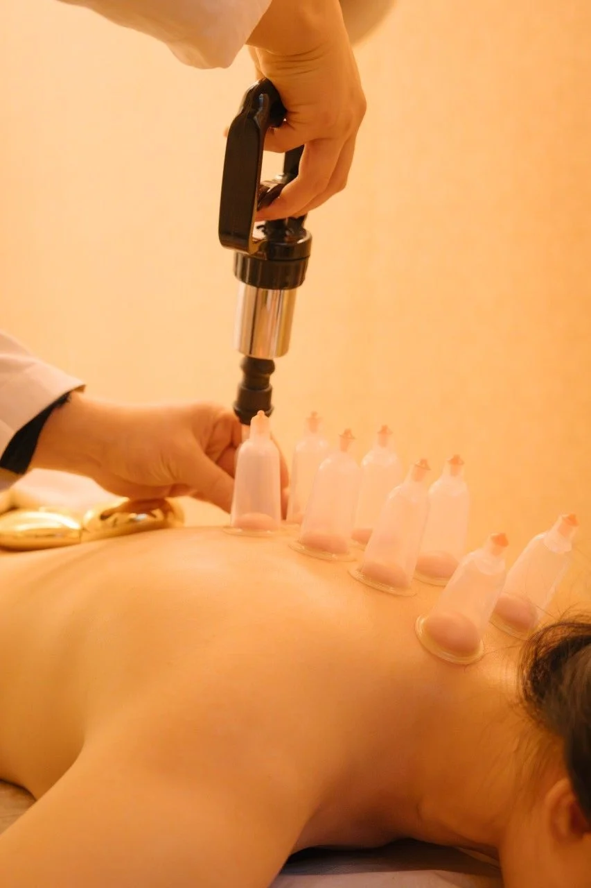 A decorative table with a lit tea light candle on a stone holder, a green glass vase with yellow flowers, and a collection of empty glass bottles on a mirror top.