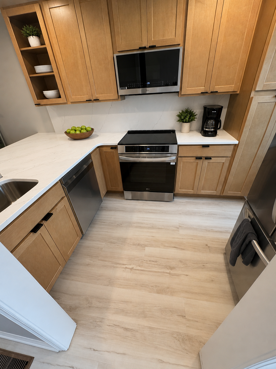 Kitchen with wooden cabinets, white countertops, stainless steel appliances, a bowl of green apples, potted plants, and a black coffee maker.