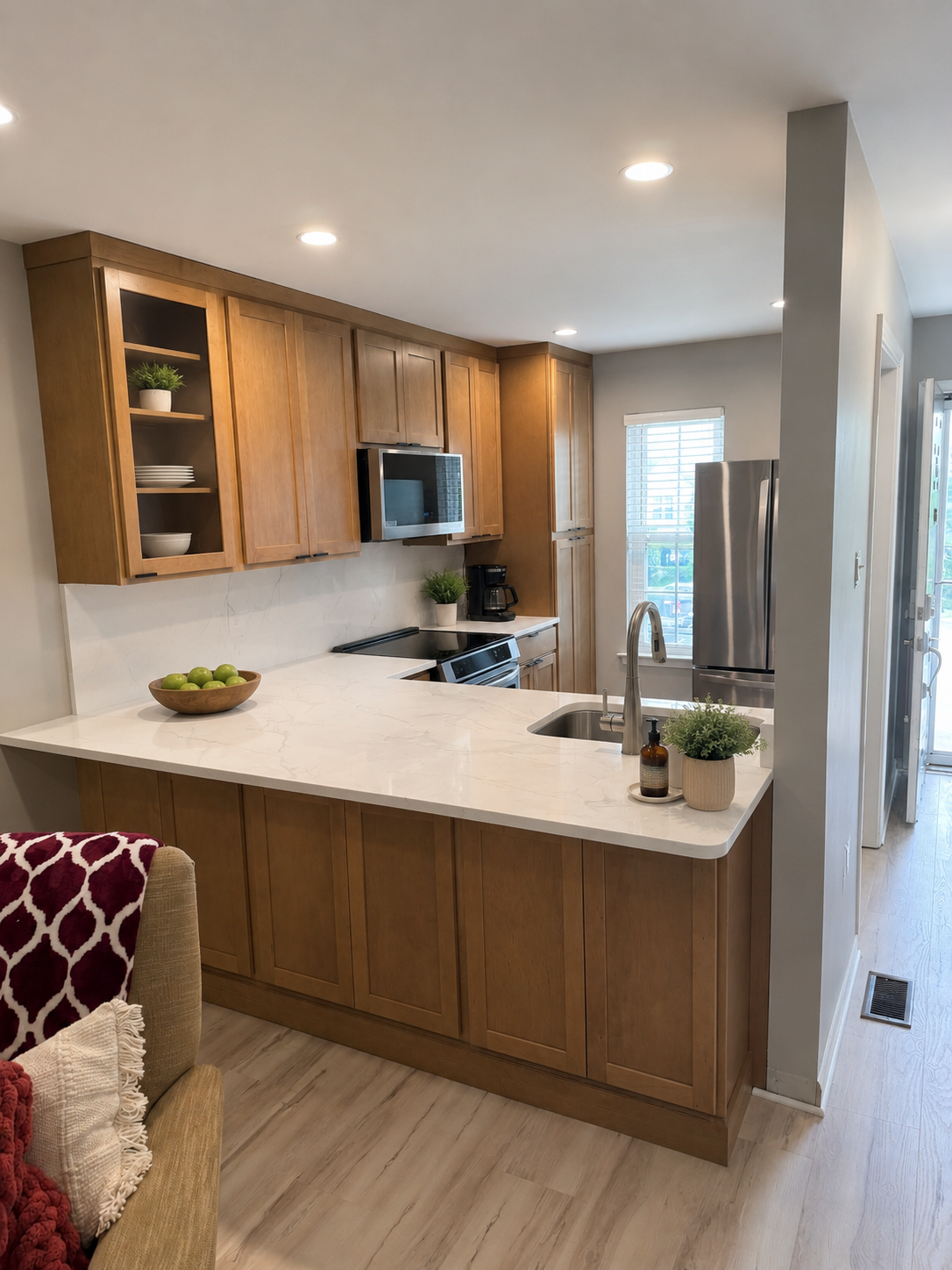 Modern kitchen with wooden cabinets, white marble countertop, stainless steel appliances, a small window, and decorative plants.