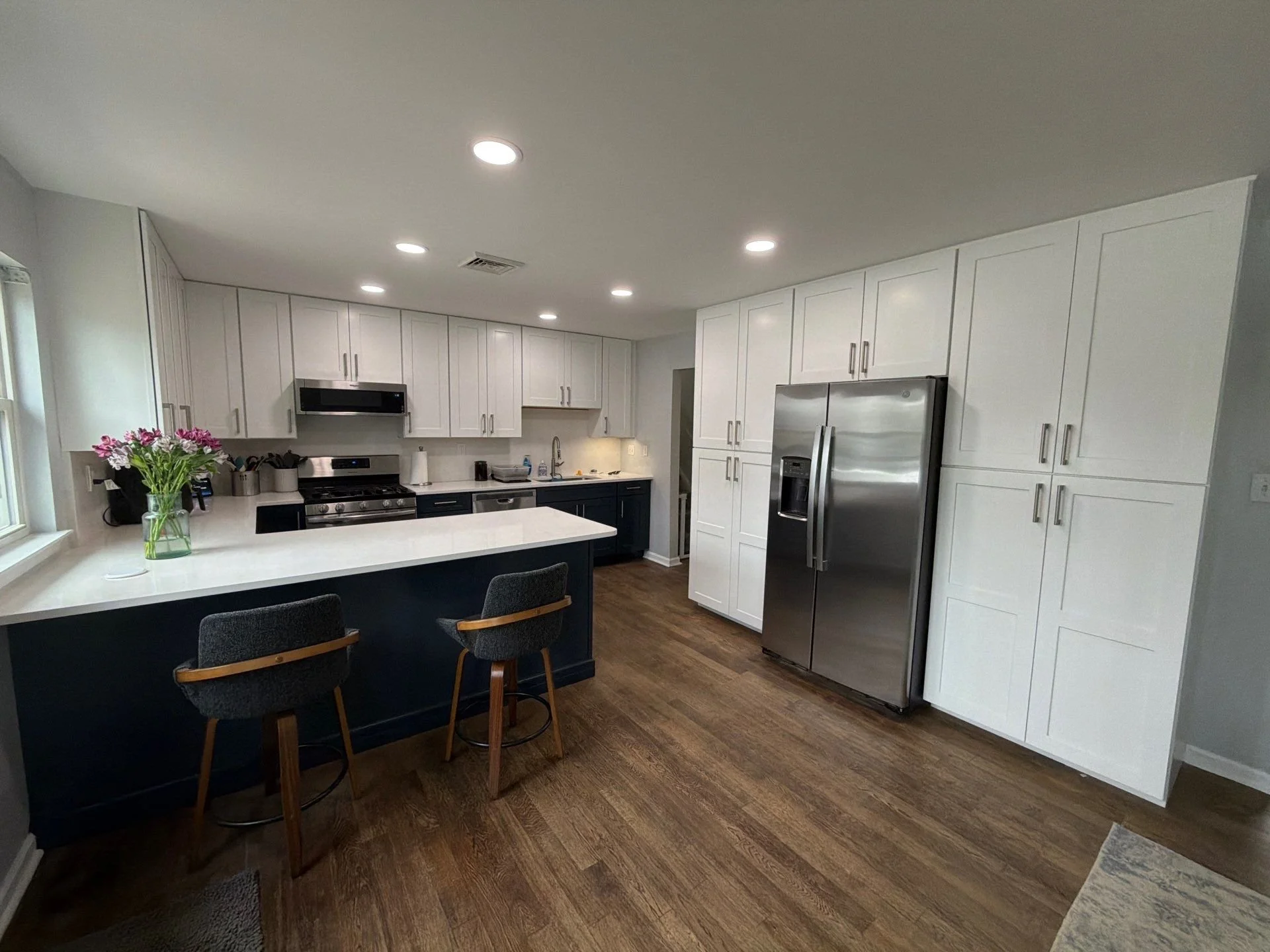 Modern kitchen with two tone cabinets shown in White and Navy Blue. Stainless steel appliances and undercabinet lighting. Refinished red oak hardwood floors.