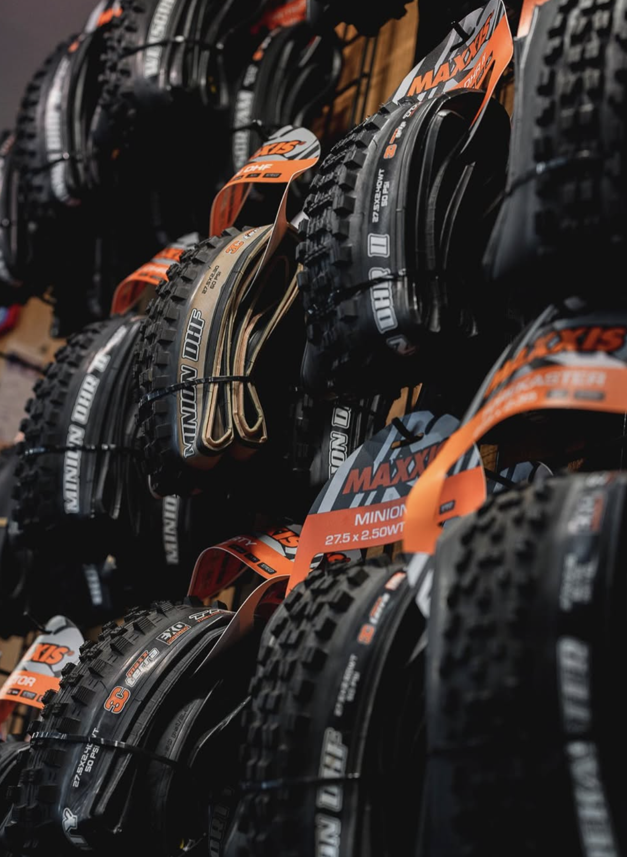 Stacked mountain bike tires with black rubber, orange labels, and metal spokes, organized on display hooks.
