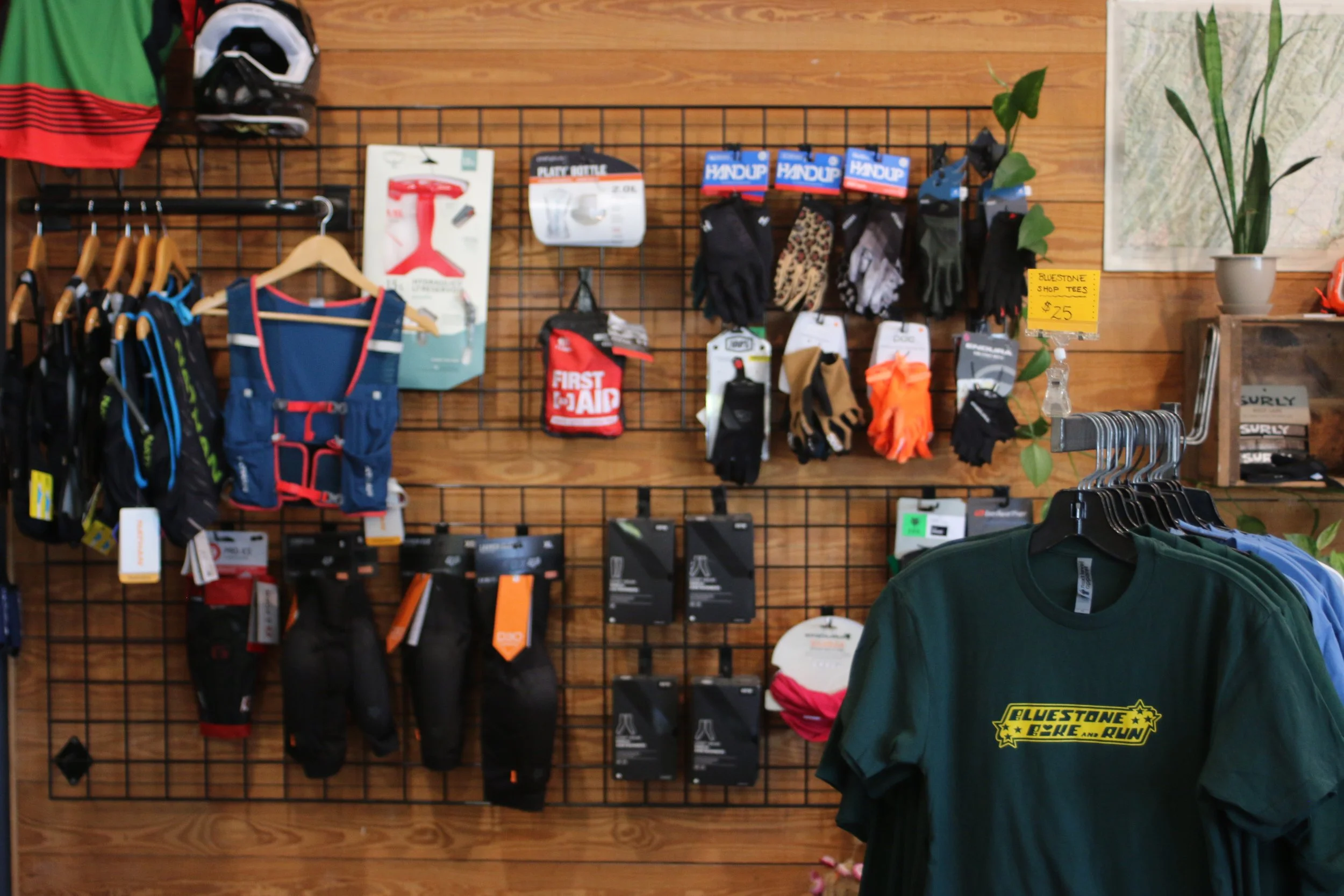 Display of outdoor and sports gear including gloves, shirts, and accessories on a wooden and metal grid wall in a retail store.