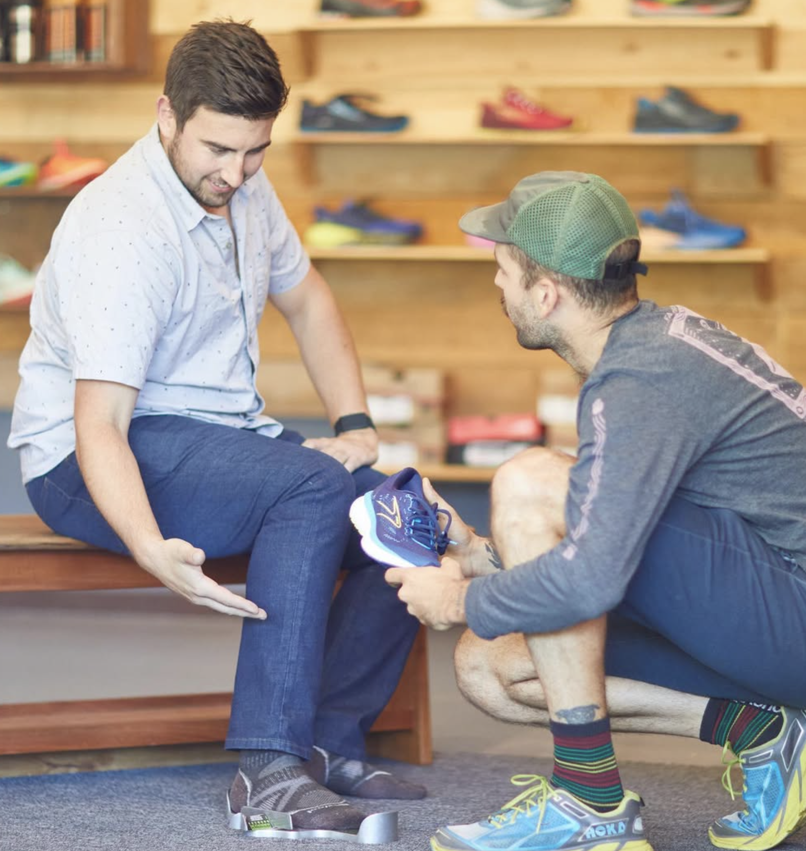 A man helping another man try on running shoes in a shoe store.