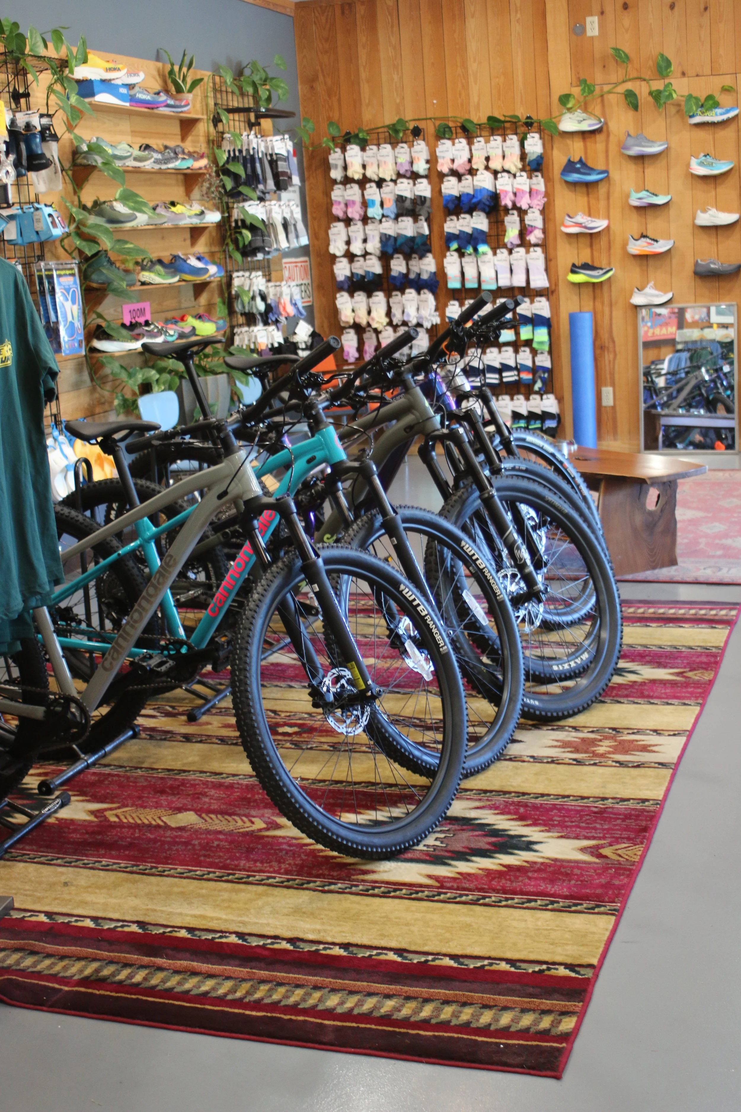 Indoor cycling shop display with several mountain bikes and shelves of shoes and accessories.