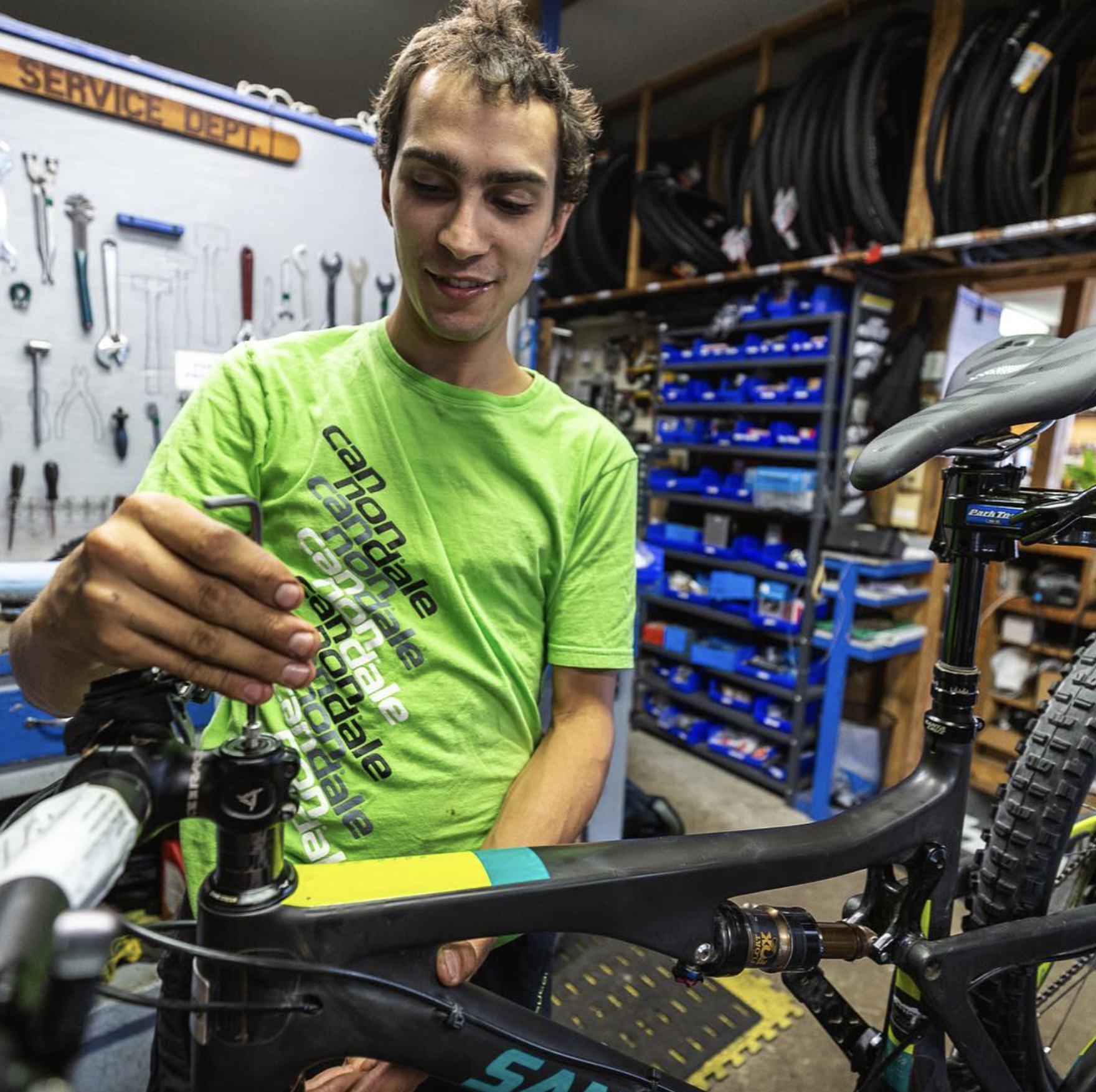 A young man in a bright green cycling shirt working on a mountain bike in a bike shop.