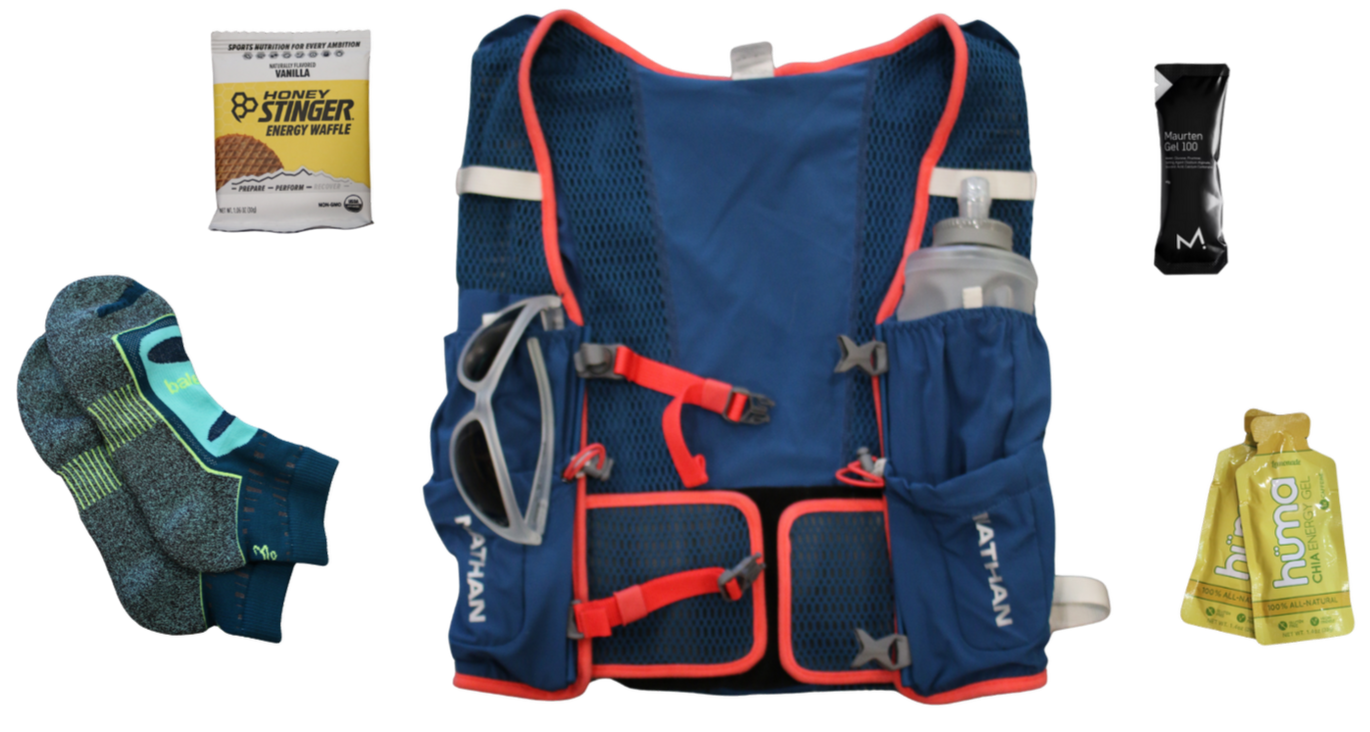 A blue hydration pack with red straps, sunglasses, and a water bottle, surrounded by energy gels and socks, on a white background.