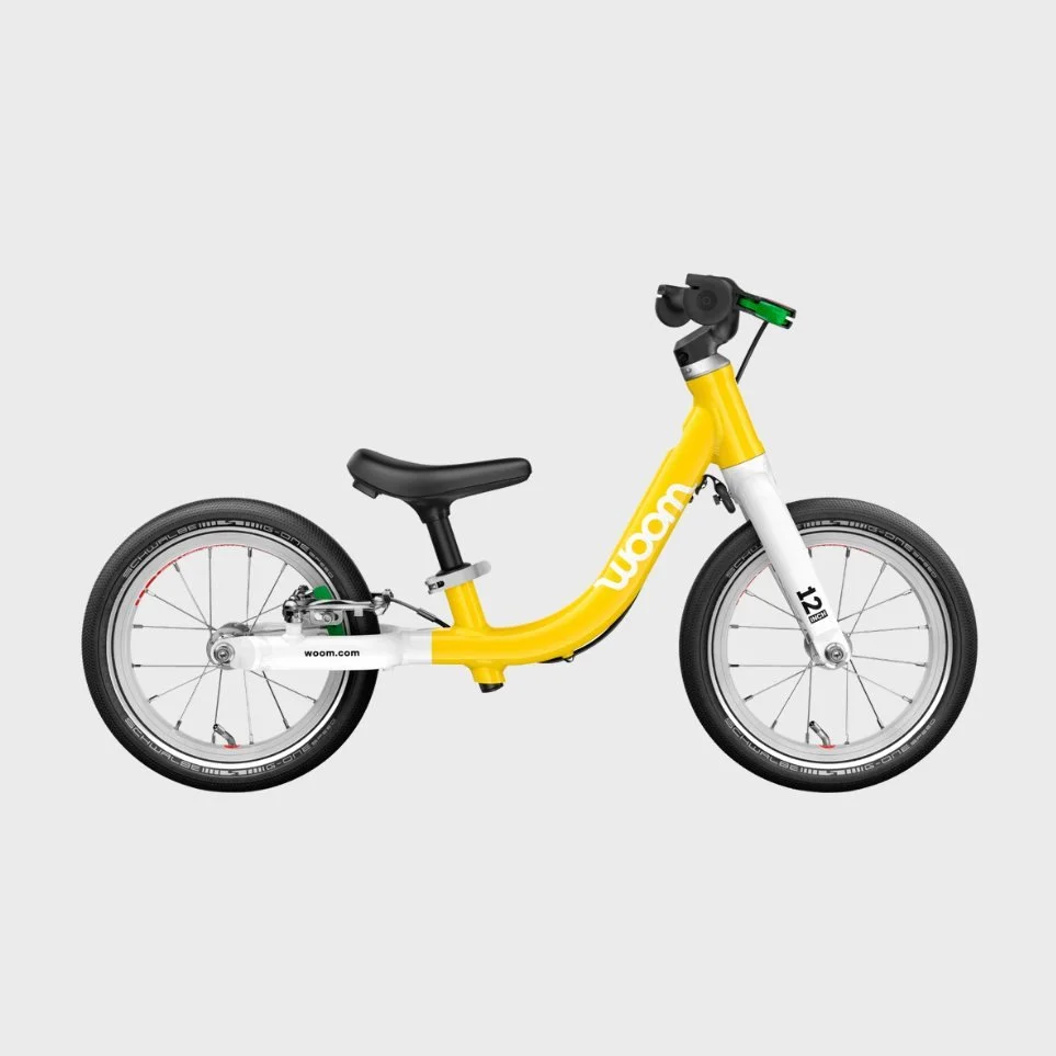 Yellow and white Woom kids' bike with black seat and wheels on a gray background.