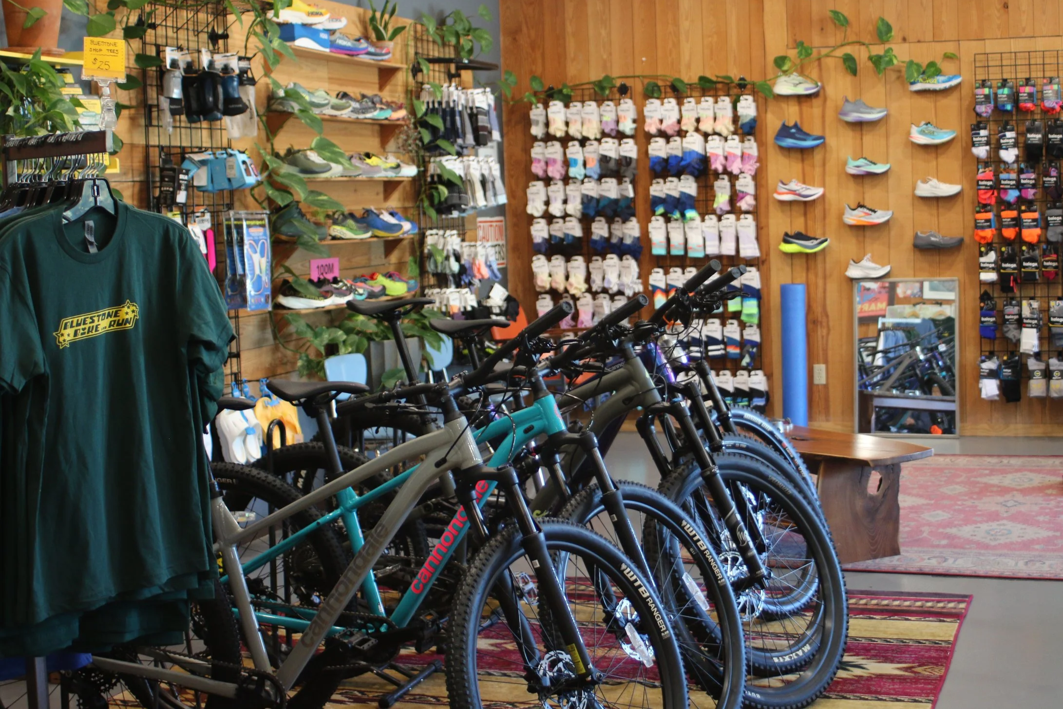 Indoor sports store display featuring recreational bicycles, sports shoes, athletic socks, and a T-shirt. Bicycles are lined up in the foreground, with a wall of shoes and socks on display in the background.
