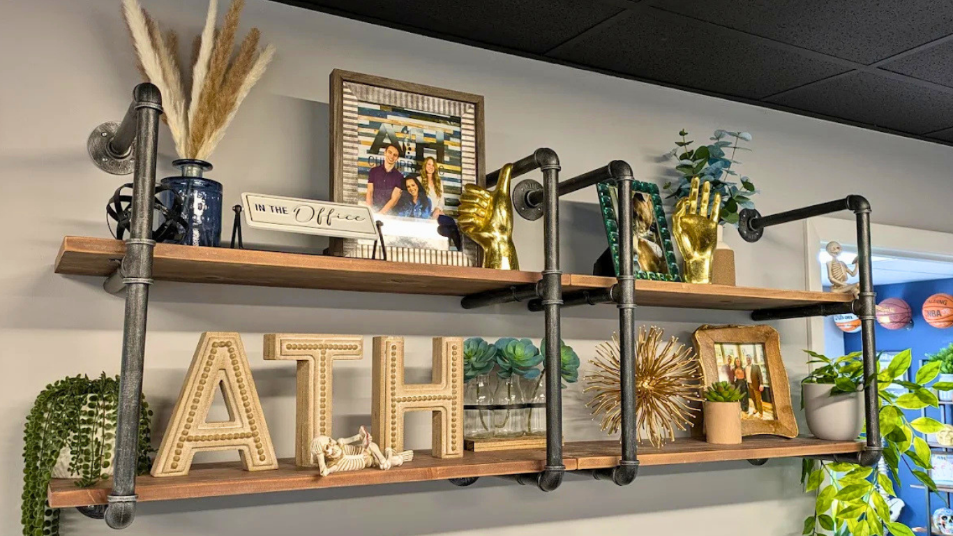 Decorative wall shelf with framed photos, plants, decorative figures, and large letters spelling 'ATH'.