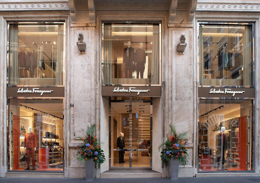 Salvatore Ferragamo store with mannequins displaying clothing inside and floral arrangements outside.