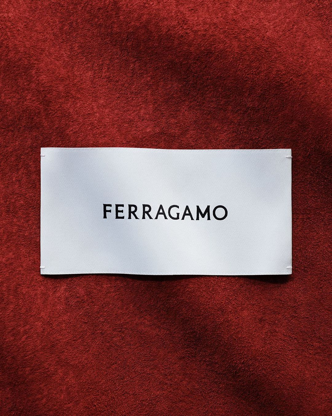 White fabric label with the brand name 'FERRAGAMO' in black lettering on a red textured background.