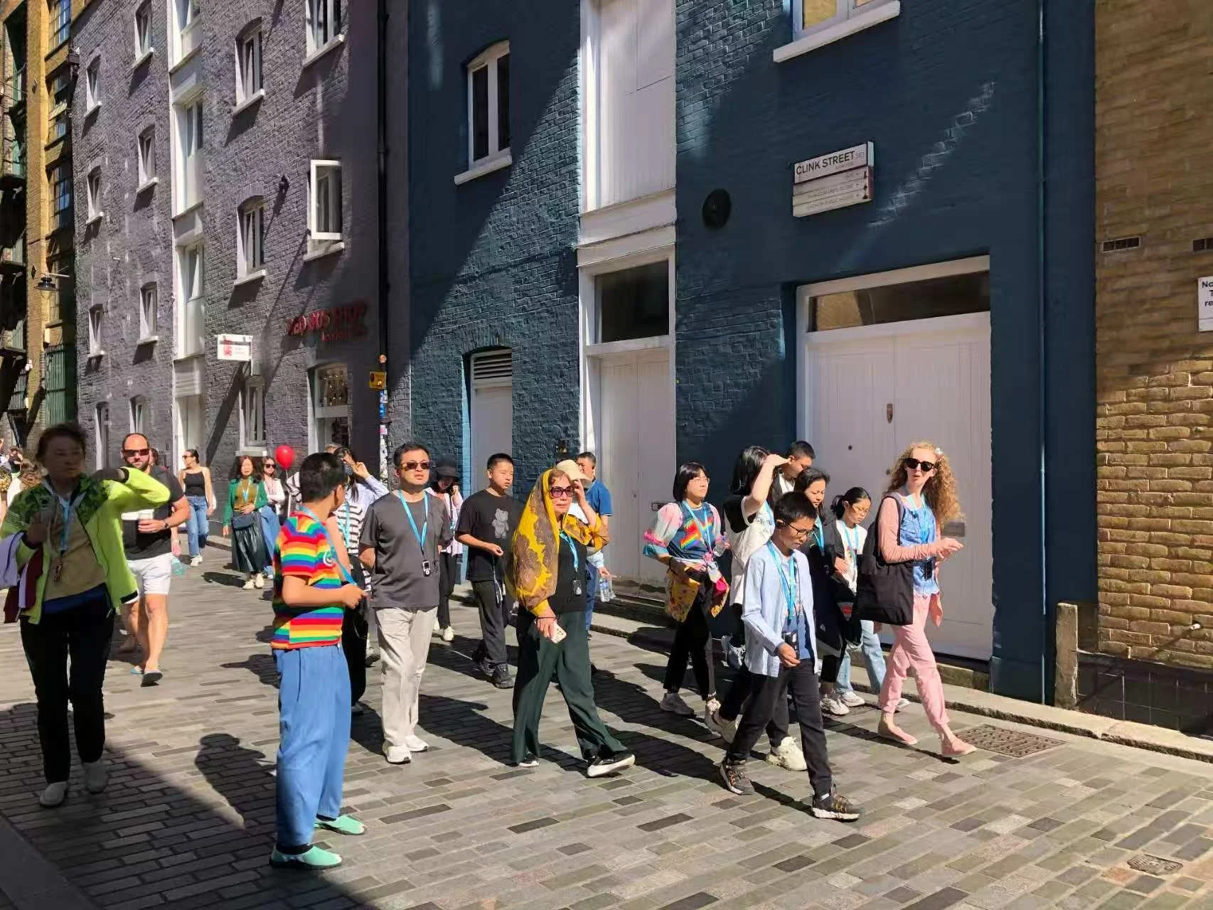 A group of diverse people walking on a cobblestone street in front of colorful buildings on a sunny day.