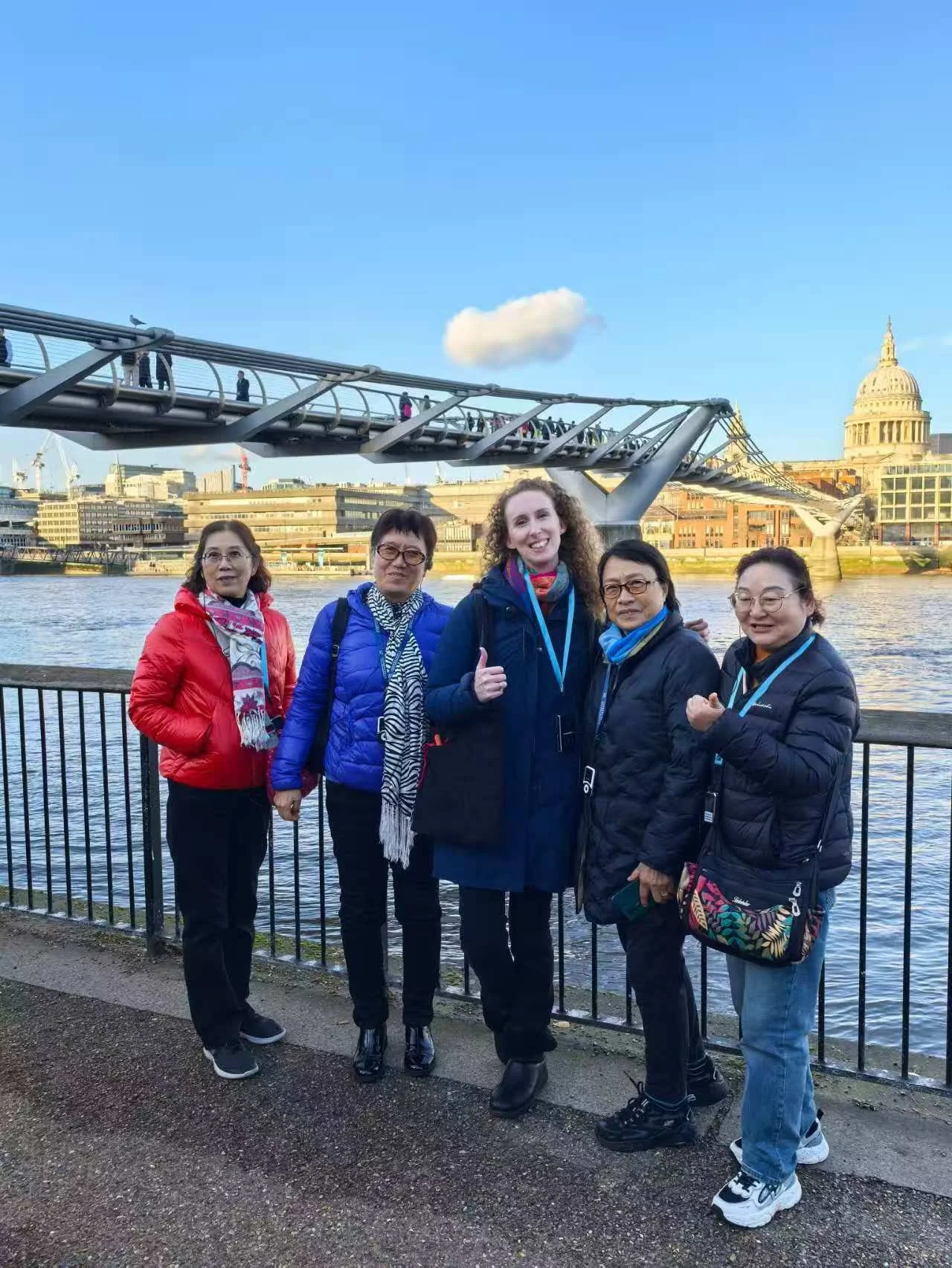 Group of five women standing by the Thames River with Millennium Bridge and St. Paul's Cathedral in London in the background.