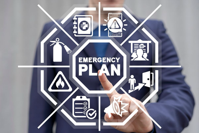 A person in a suit pointing at a digital emergency plan diagram with icons related to safety procedures, alerts, firefighting, medical assistance, and communications.