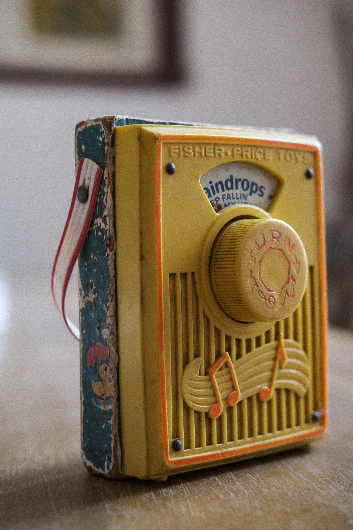 A vintage Fisher-Price toy radio with a yellow front, orange and musical note design, and a volume knob labeled 'TUNE' on a wooden surface.