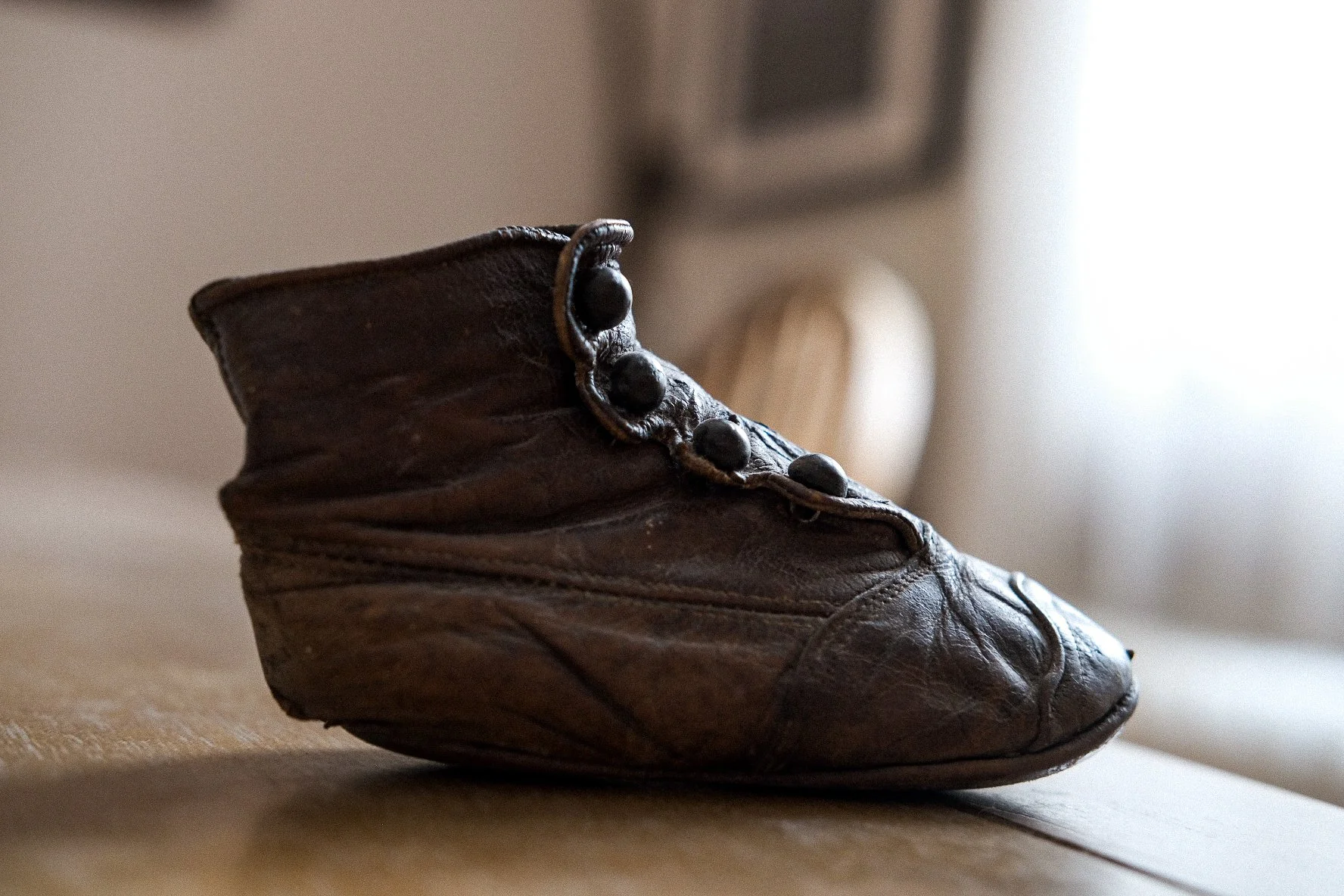 Close-up of a worn, brown leather cowboy boot with decorative metal rivets on the side, placed on a wooden surface with a blurred interior background.