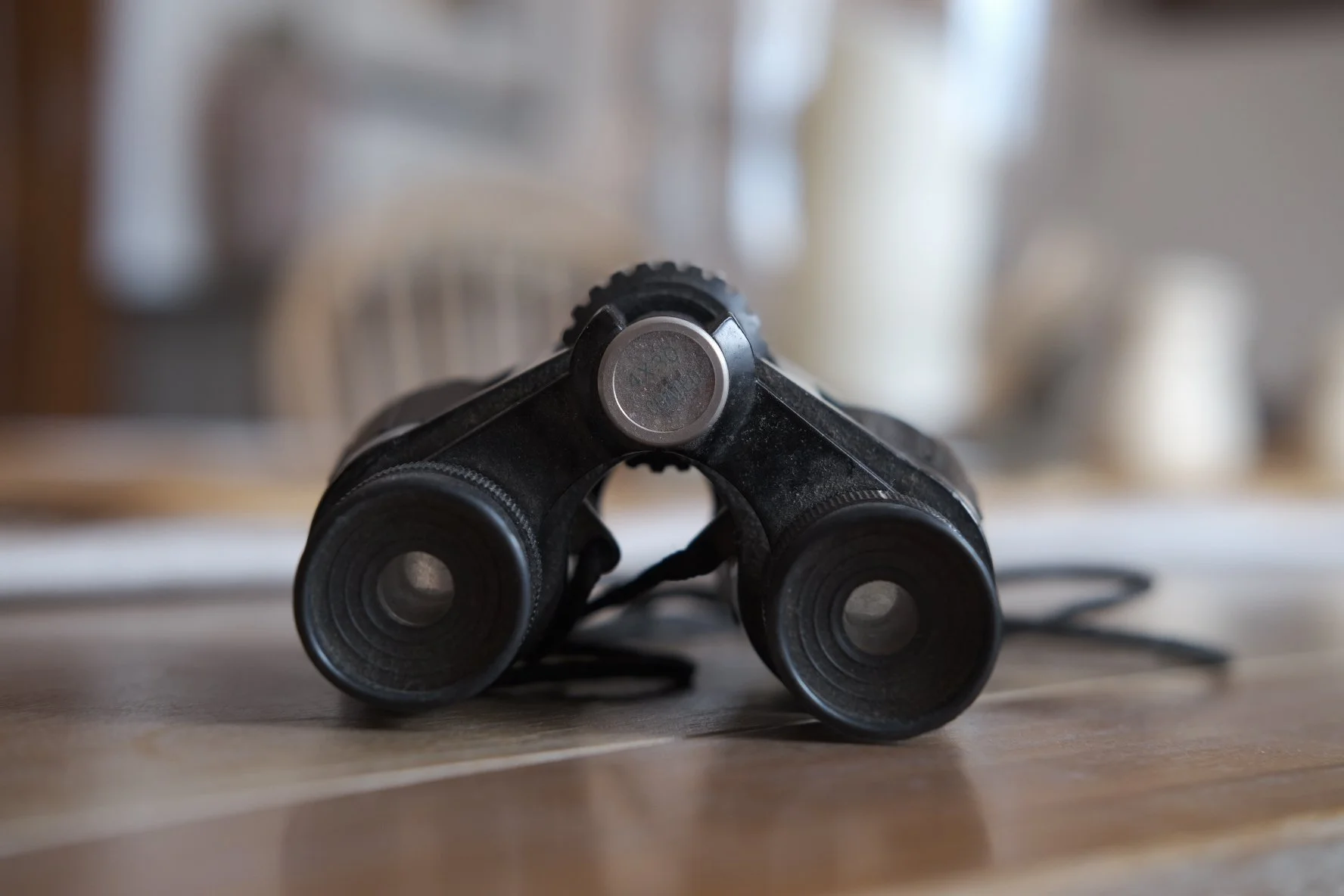 Close-up of black binoculars on a wooden surface with a blurred background.