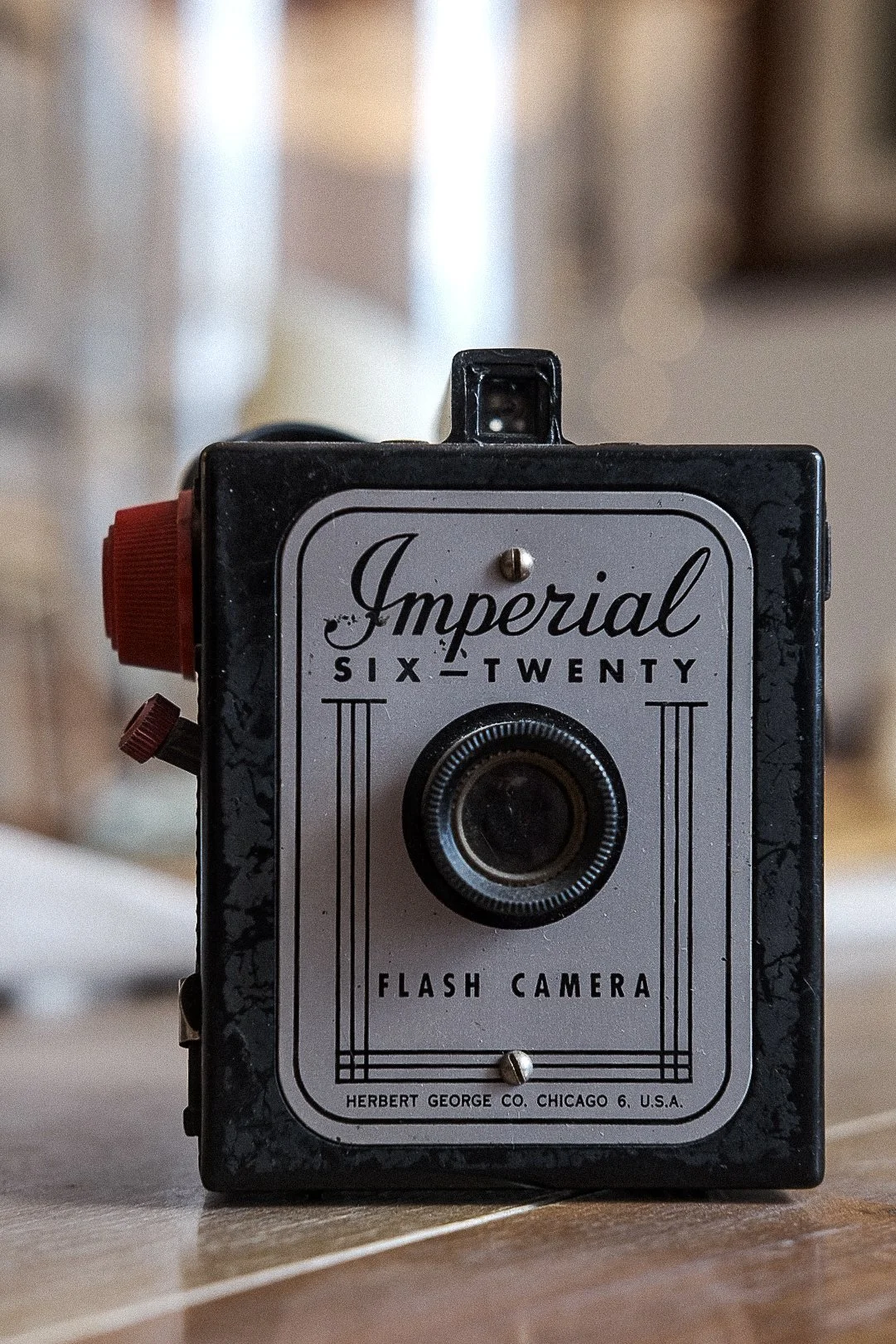 Vintage Imperial Six-Twenty flash camera with a red side knob and black body, standing on a wooden surface.