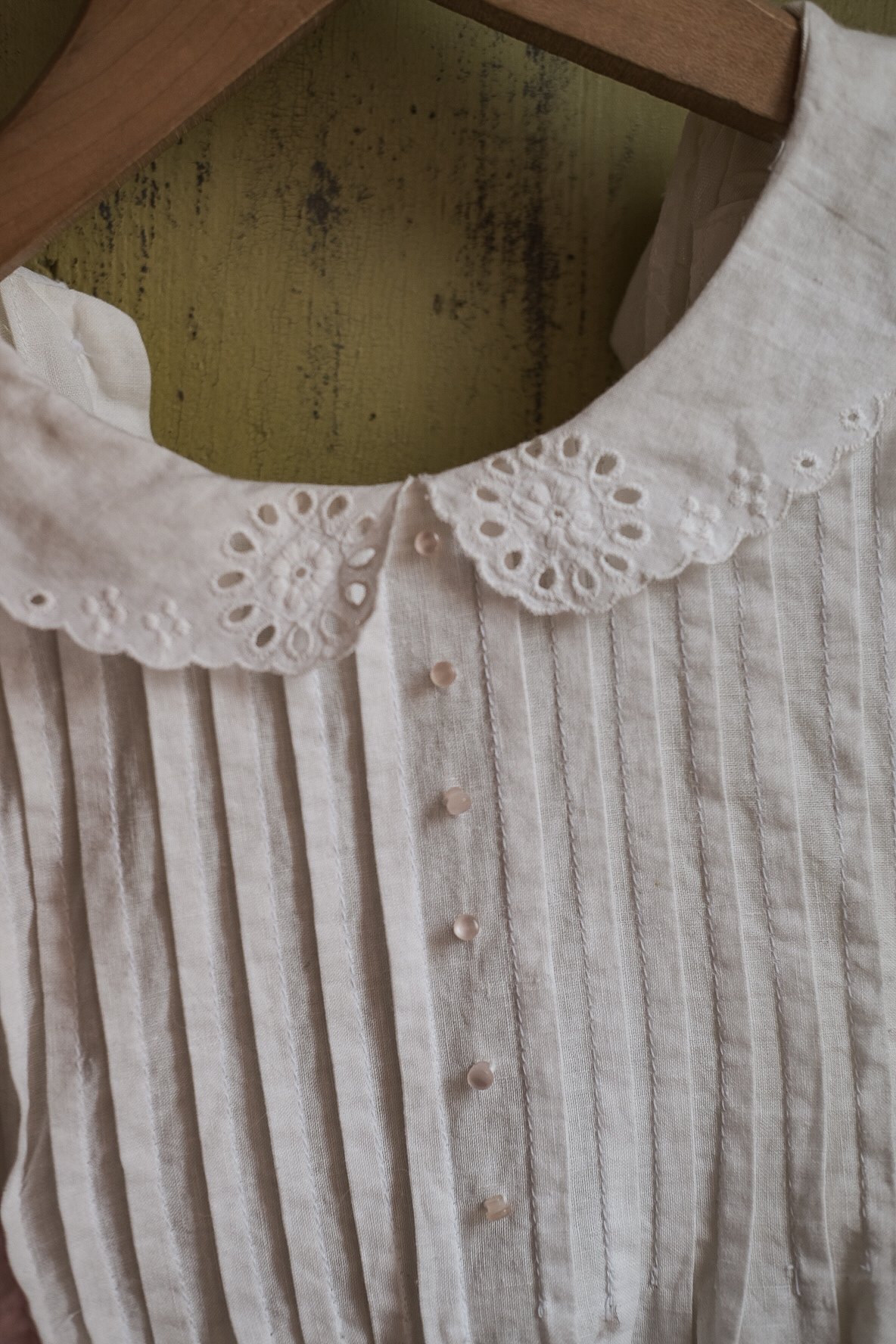 Close-up of a white striped blouse with embroidered eyelet collar and small buttons.