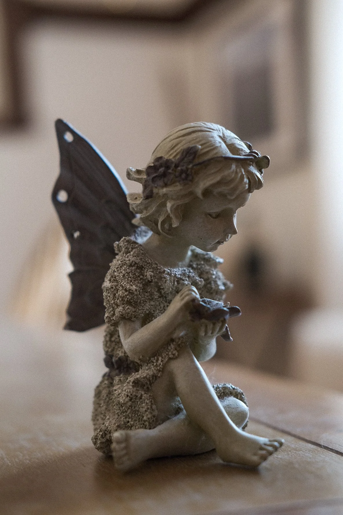 A decorative figurine of a fairy girl with butterfly wings, sitting on the floor, with her legs crossed and looking down thoughtfully.