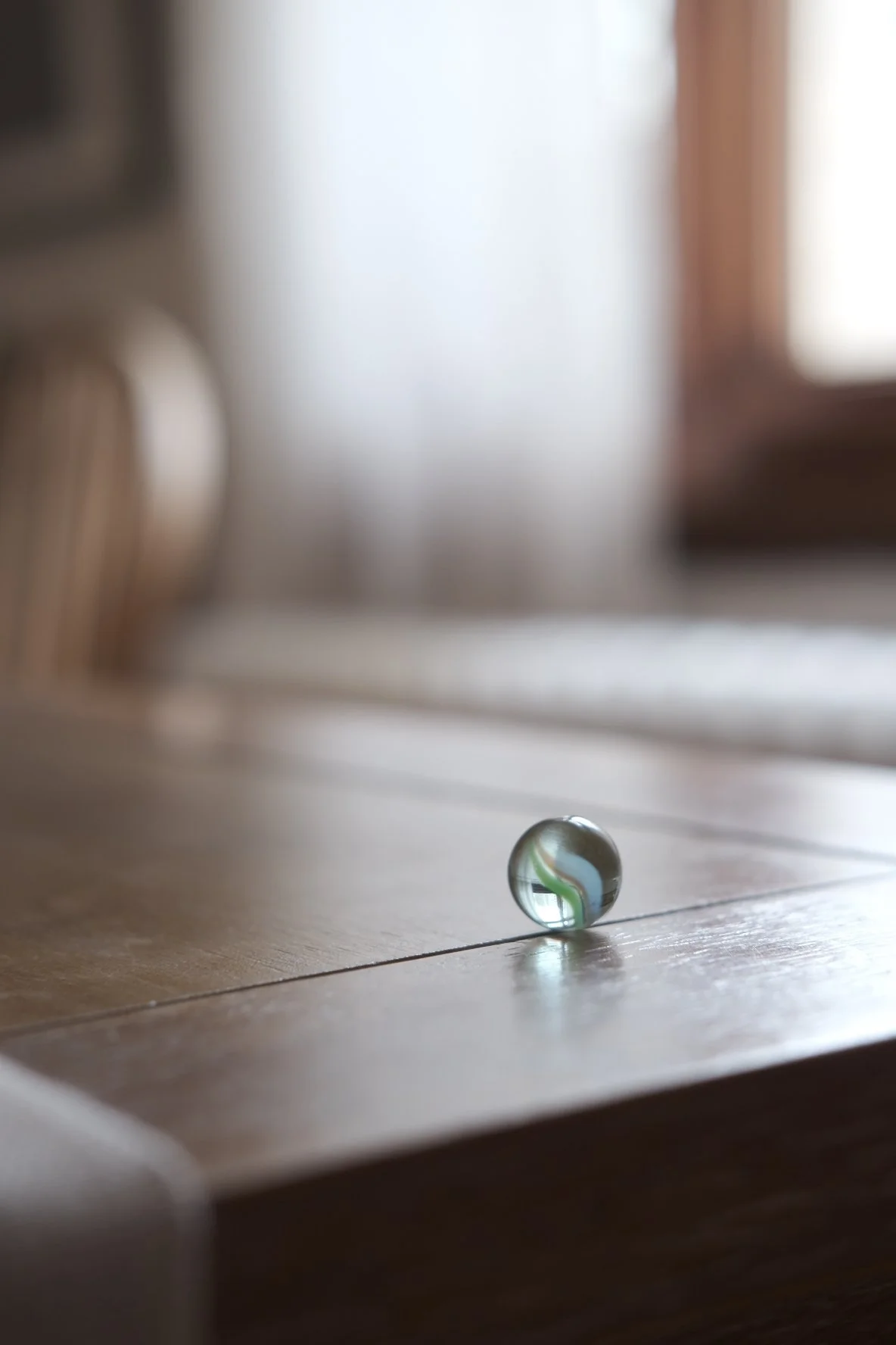 A marble on a wooden floor with reflections and blurred background.