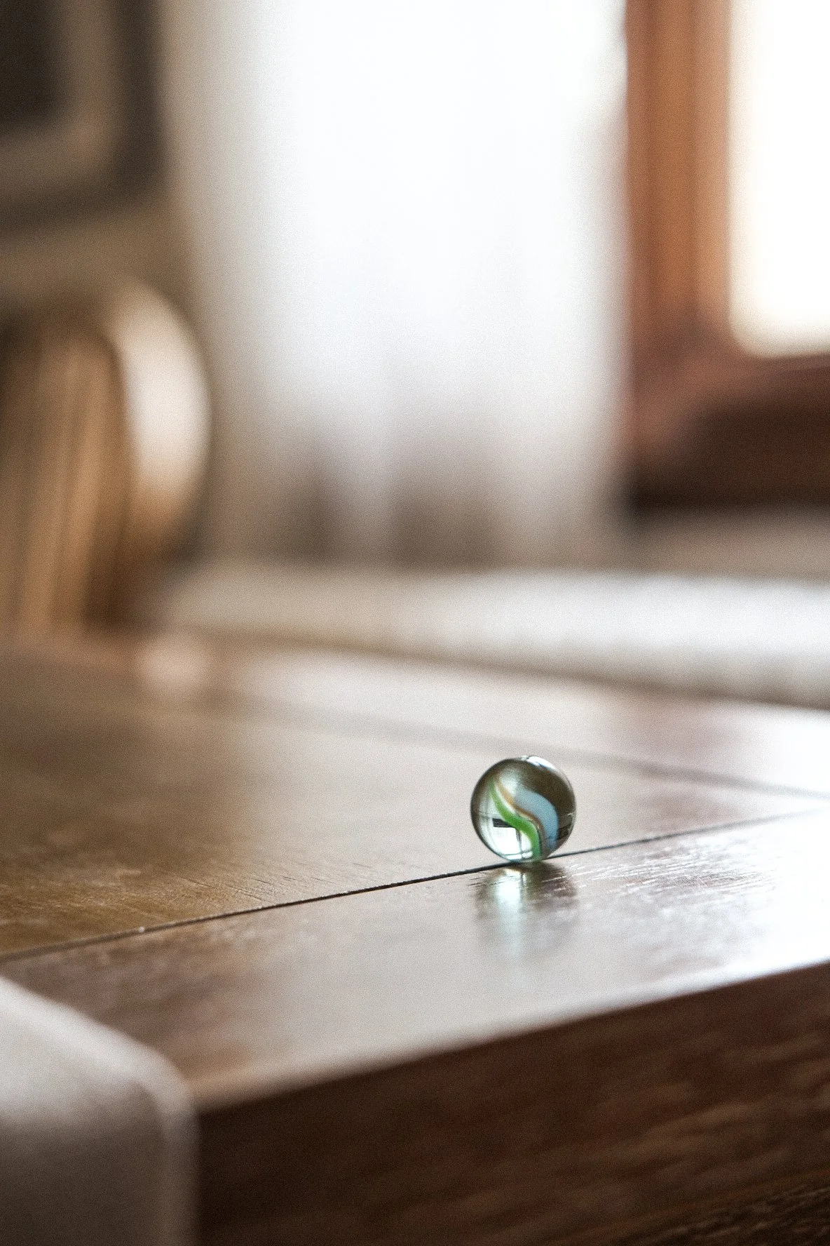 A glass marble on a wooden surface with a blurred background of interior lighting and furniture.