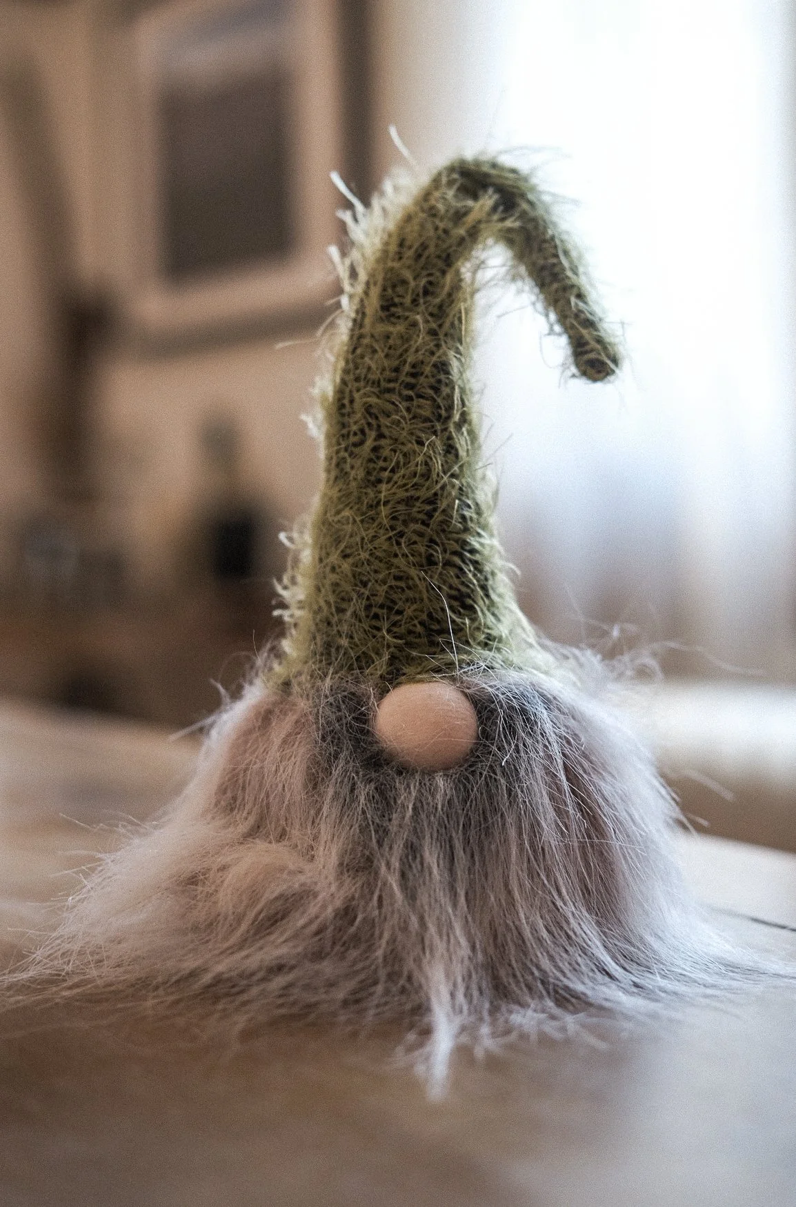 Close-up of a rabbit's nose, chin, and curly whiskers, with a tall, fuzzy tail upright behind its head, on a wooden floor with blurred background.