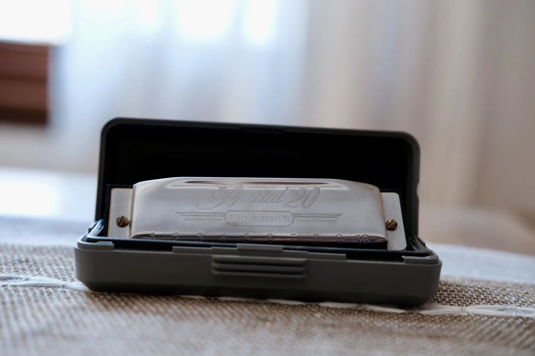 A vintage Harmonica in a black case placed on a fabric surface, with a blurred background.