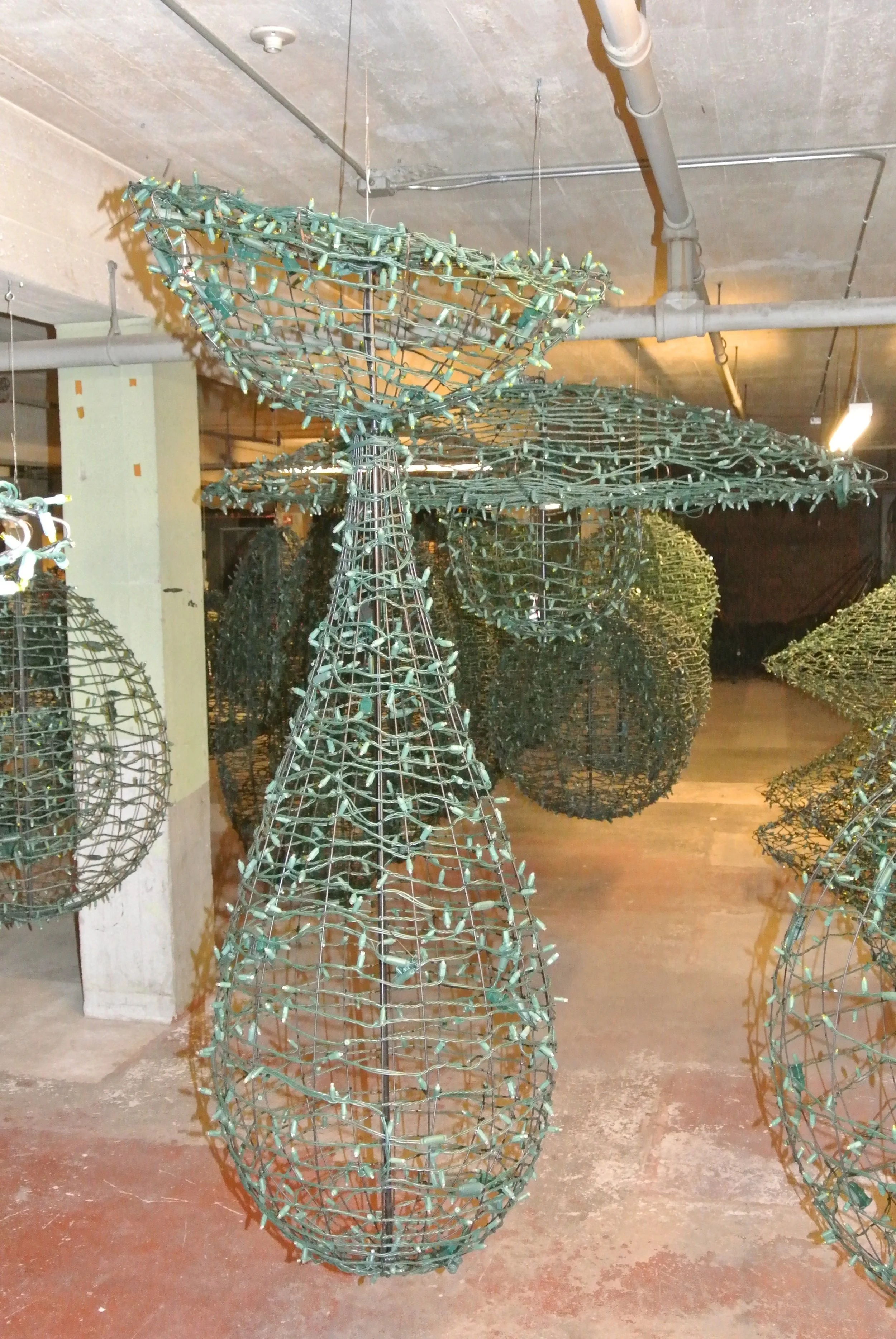 Metal wireframe sculpture of an umbrella, teardrop-shaped with a circular top, displayed hanging from the ceiling in a room with other spherical wireframe sculptures.