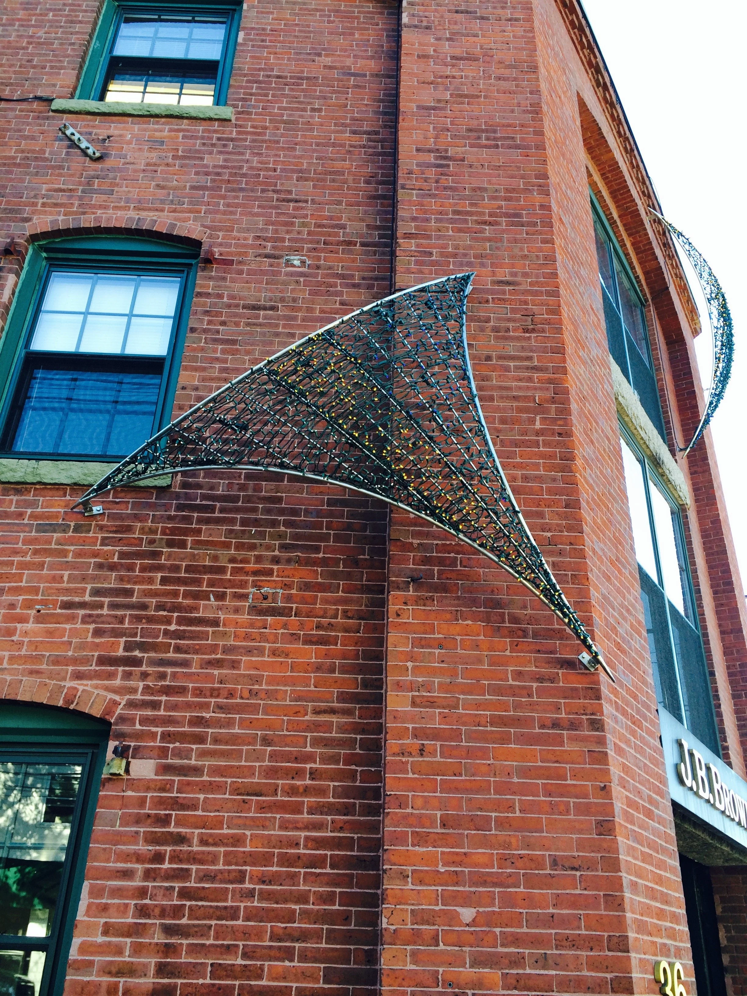 Decorative illuminated metal canopy on the exterior corner of a brick building.