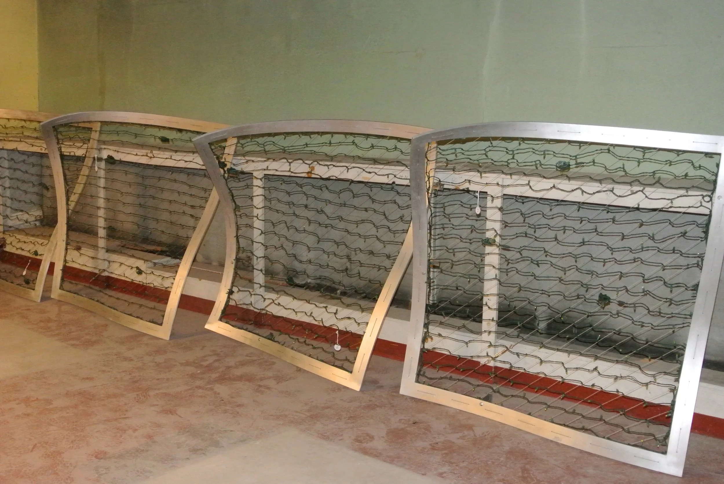 Five metal window frames with grid-like wires inside, leaning against a wall on a tiled floor.