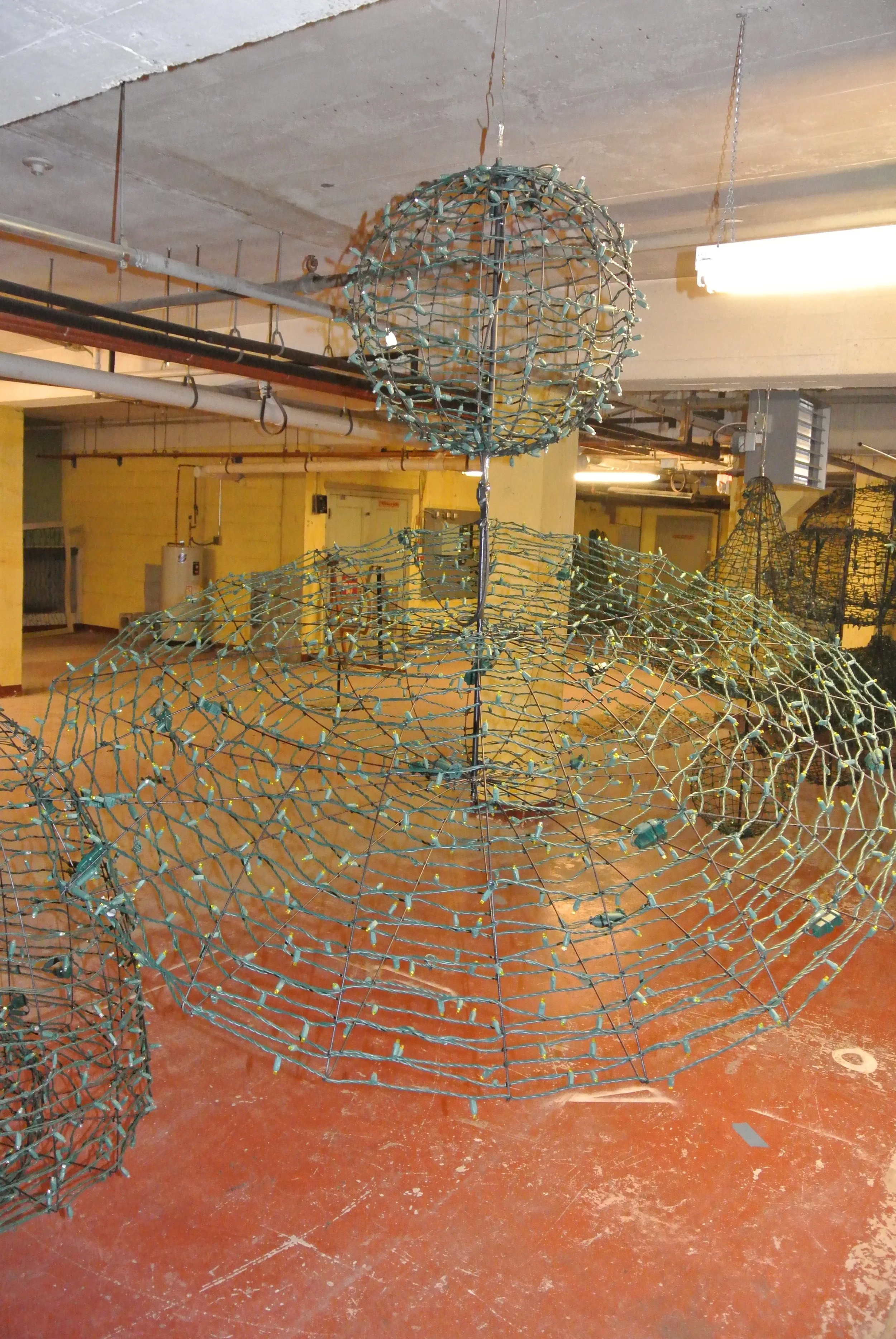 Large metal wire sculptures of spheres and conical shapes, resembling abstract or industrial art, inside a warehouse or industrial space with exposed concrete ceilings and pipes.