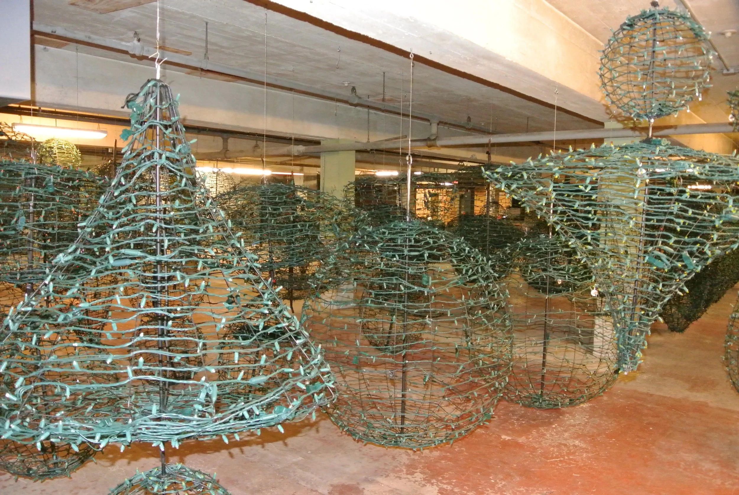 Multiple metal wireframe shapes resembling bells or abstract sculptures hanging from the ceiling in an industrial-style space.