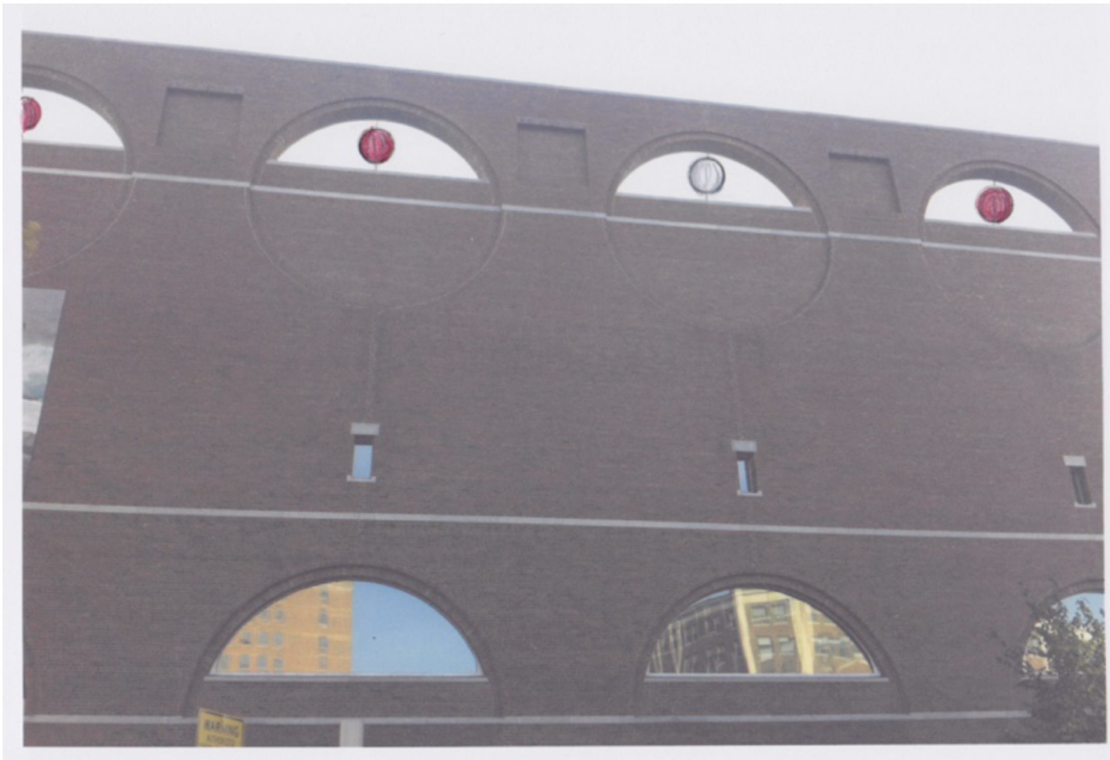 A brick building with three large arched windows on the top and two smaller arched windows on the bottom. Red and white lanterns hang in the top arches. The bottom windows reflect surrounding buildings and sky.