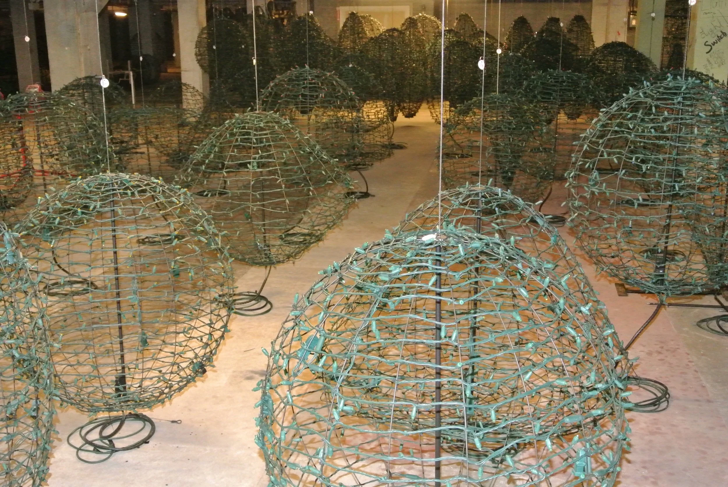 Multiple wireframe metal lanterns arranged in rows on the floor in a display area.