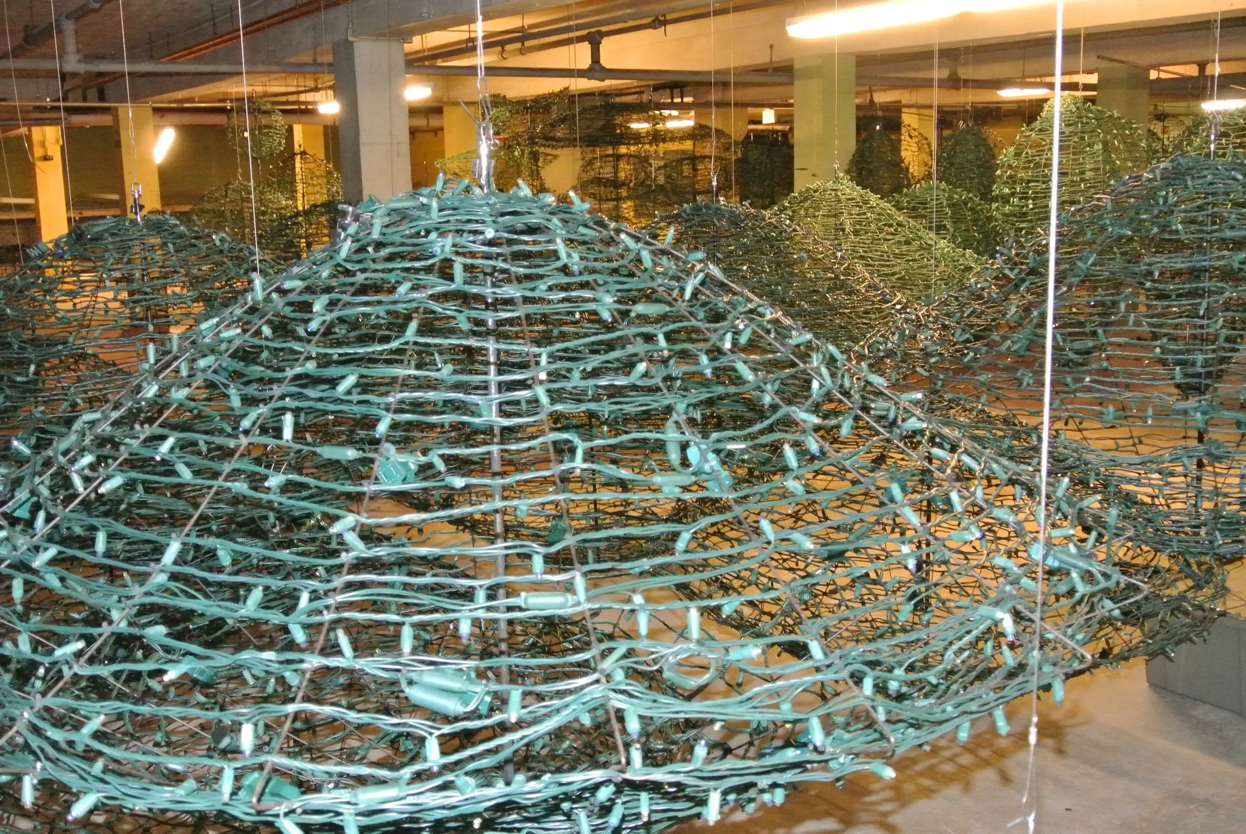 A large sculpture made of green holiday string lights shaped like a mountain or hill, displayed indoors in an art gallery or museum.