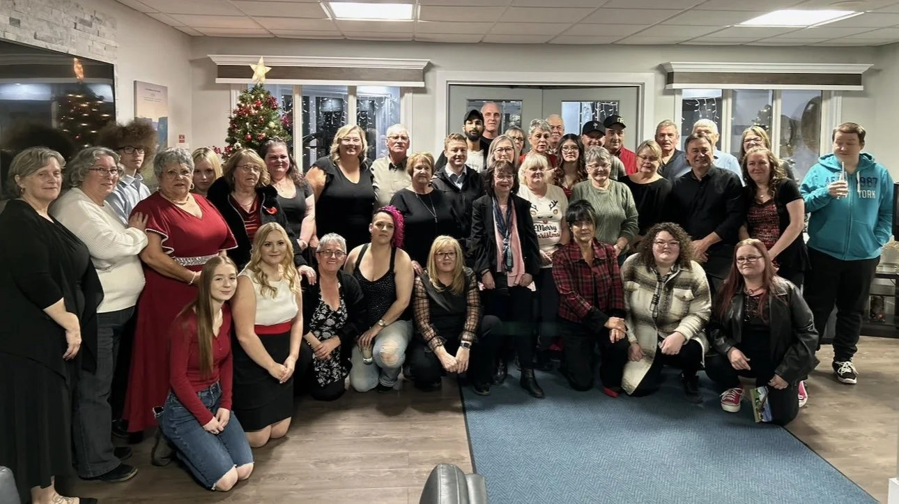 Group of people gathered indoors for a holiday celebration, with a decorated Christmas tree in the background.