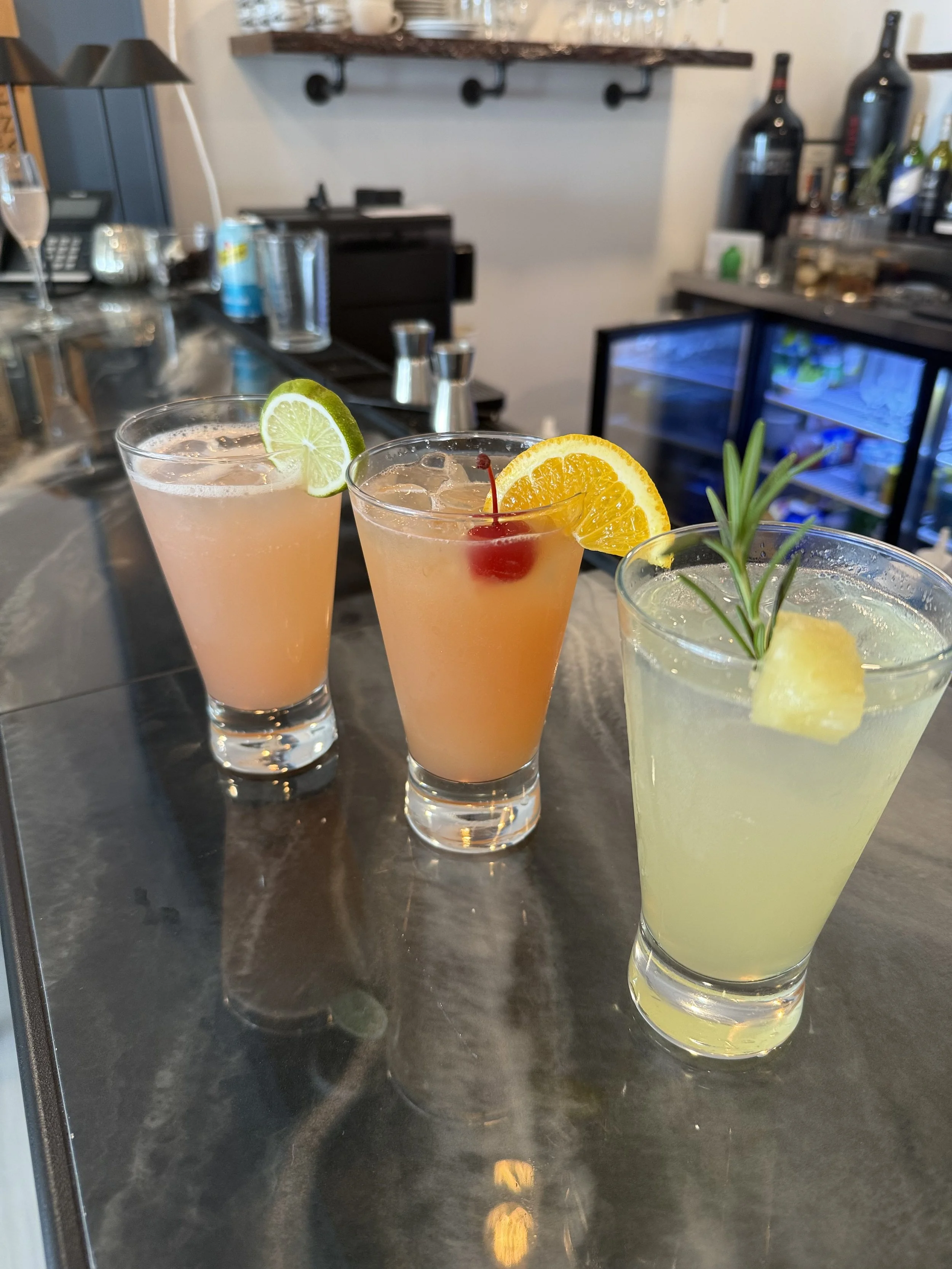 Three colorful cocktails with garnishes on a bar counter.