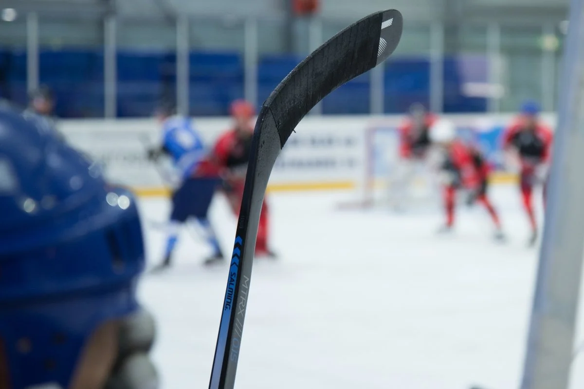 Close up shot of hockey stick with blurry hockey game in the background