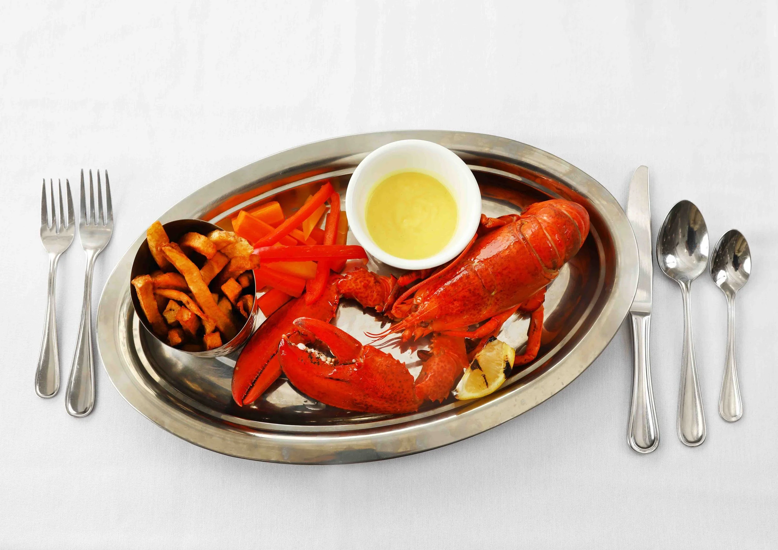 Lobster with lemon, fries, and sliced red and yellow bell peppers on a metal platter
