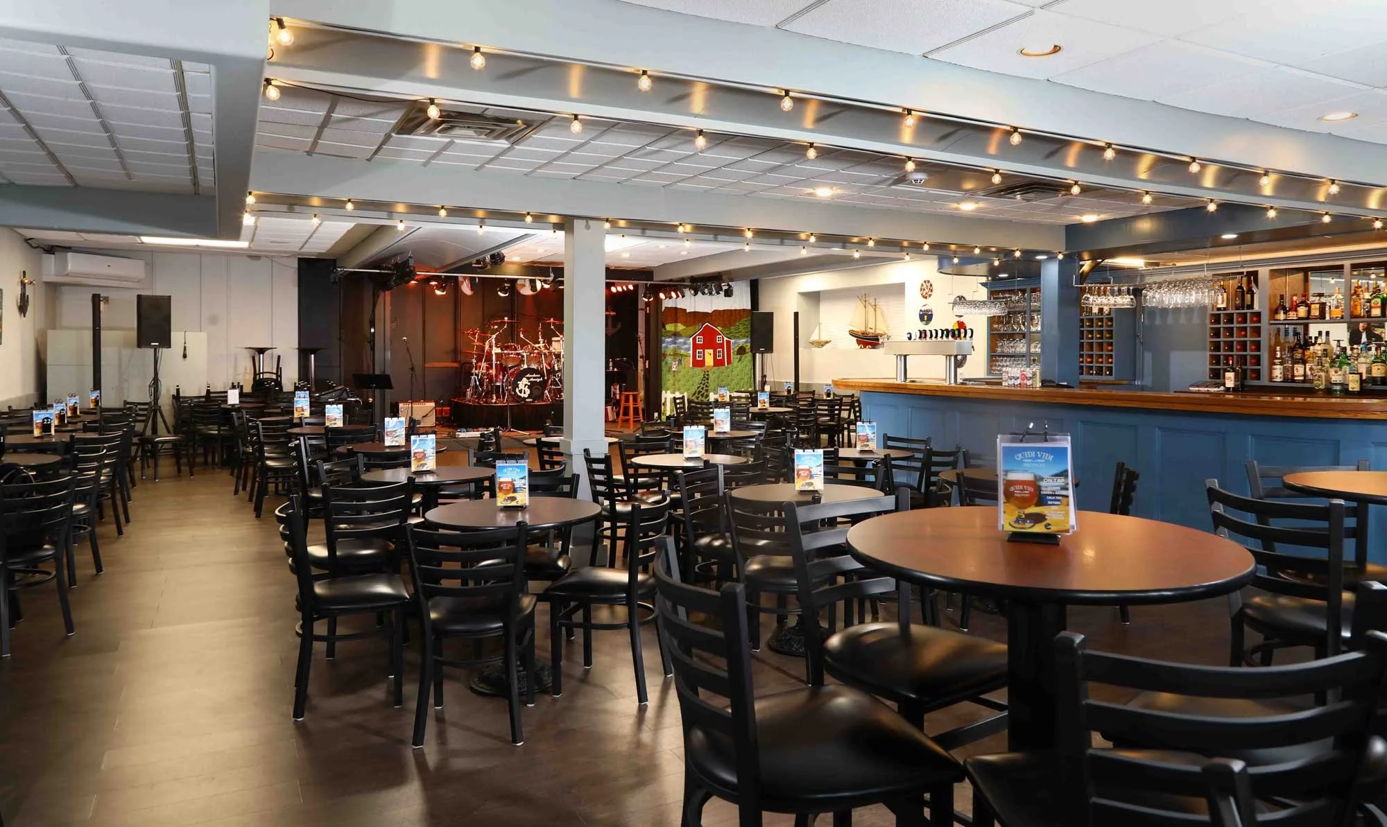 Empty indoor bar and dining area with tables, chairs, and a stage with musical instruments.