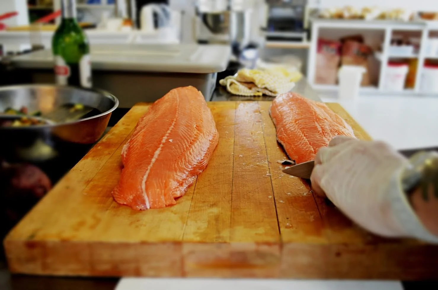Two fillets of raw salmon on a wooden cutting board in a kitchen.