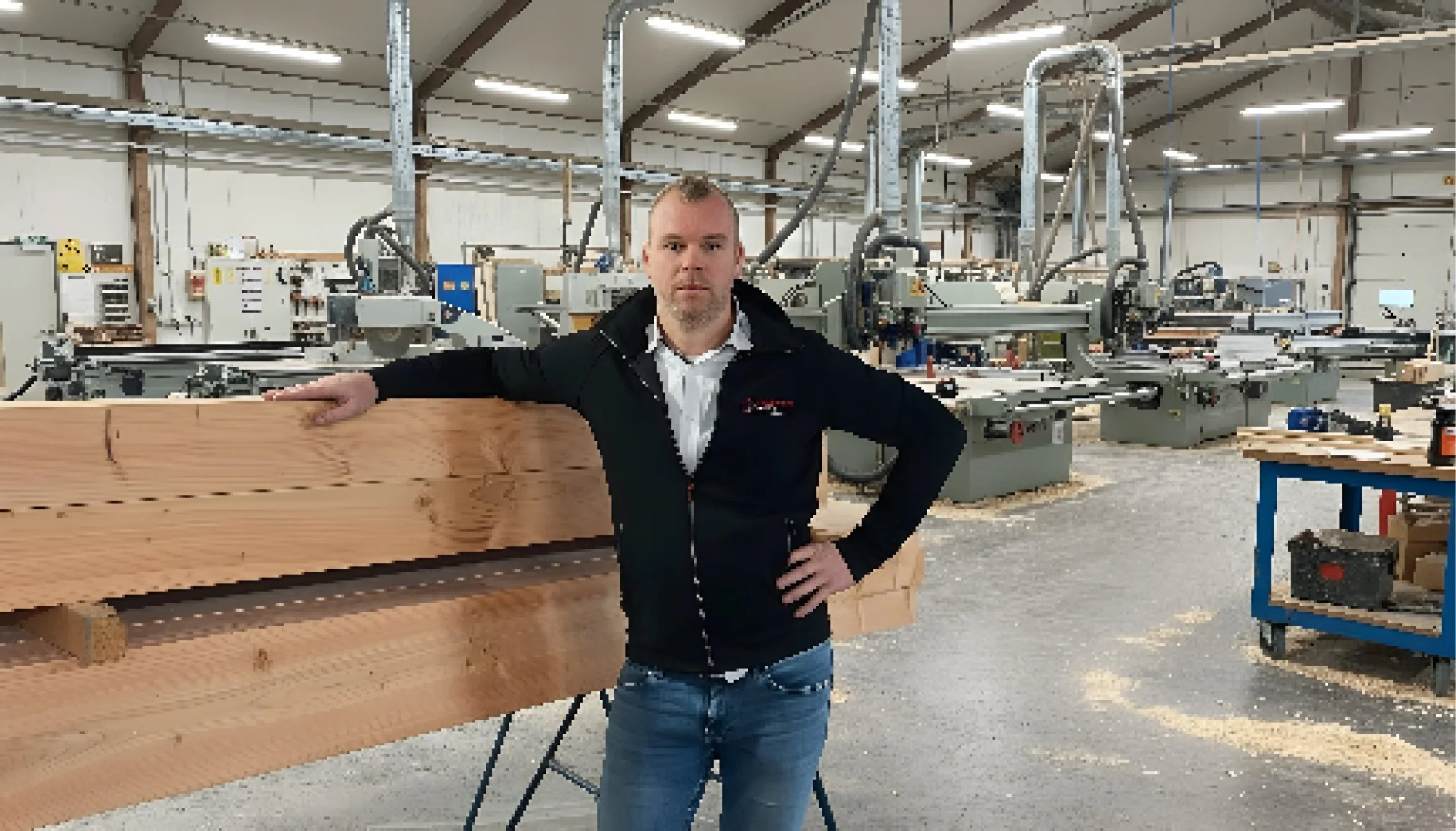Man in een houtwerkplaats, omgeven door machines en houtblokken.