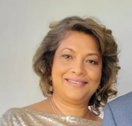 A smiling woman with shoulder-length hair, wearing a beige, sparkly top, against a light-colored background.